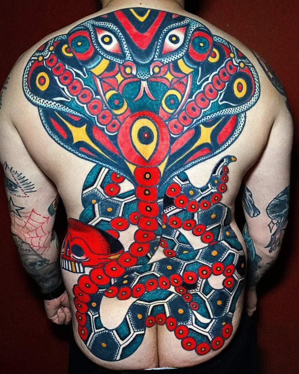 Colorful tattoo of a stylized octopus and snake on a person's back, with vibrant red, yellow, black, and blue ink.
