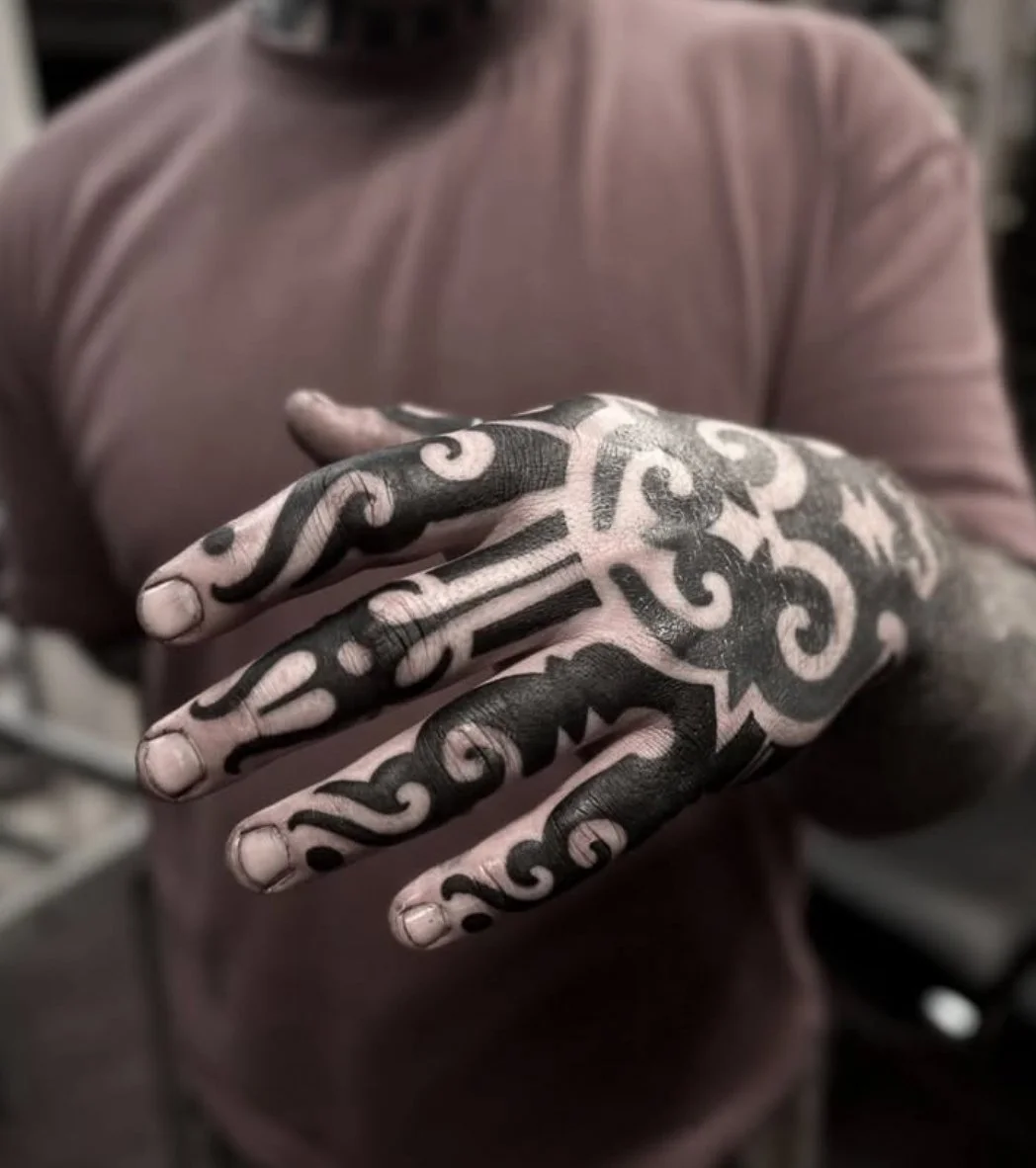 A person with intricate black and white tattoo designs on their hand and fingers, wearing a pinkish shirt.