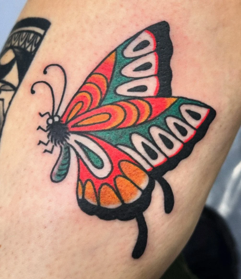 Colorful butterfly tattoo with orange, green, red, and white wings on skin.