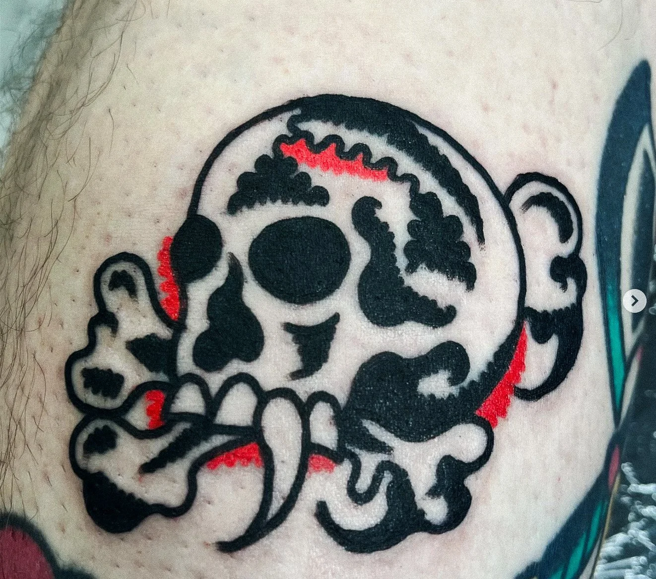 Tattoo of a skull with a dollop and bones on the face, using black and red ink.