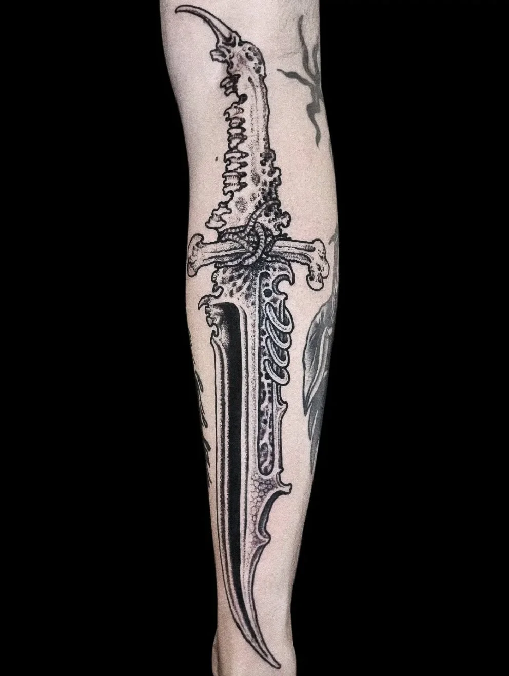 Black and gray tattoo of a fantasy-style sword with intricate details on a person's forearm.
