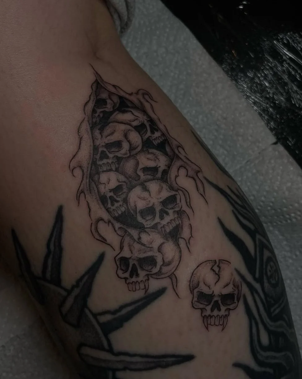 Tattoo of multiple skulls with flames and dark shading on skin.