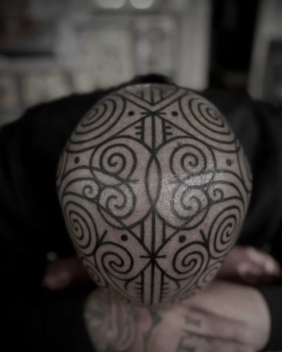 Person holding a spherical object with intricate black tribal or geometric tattoo patterns covering its surface.