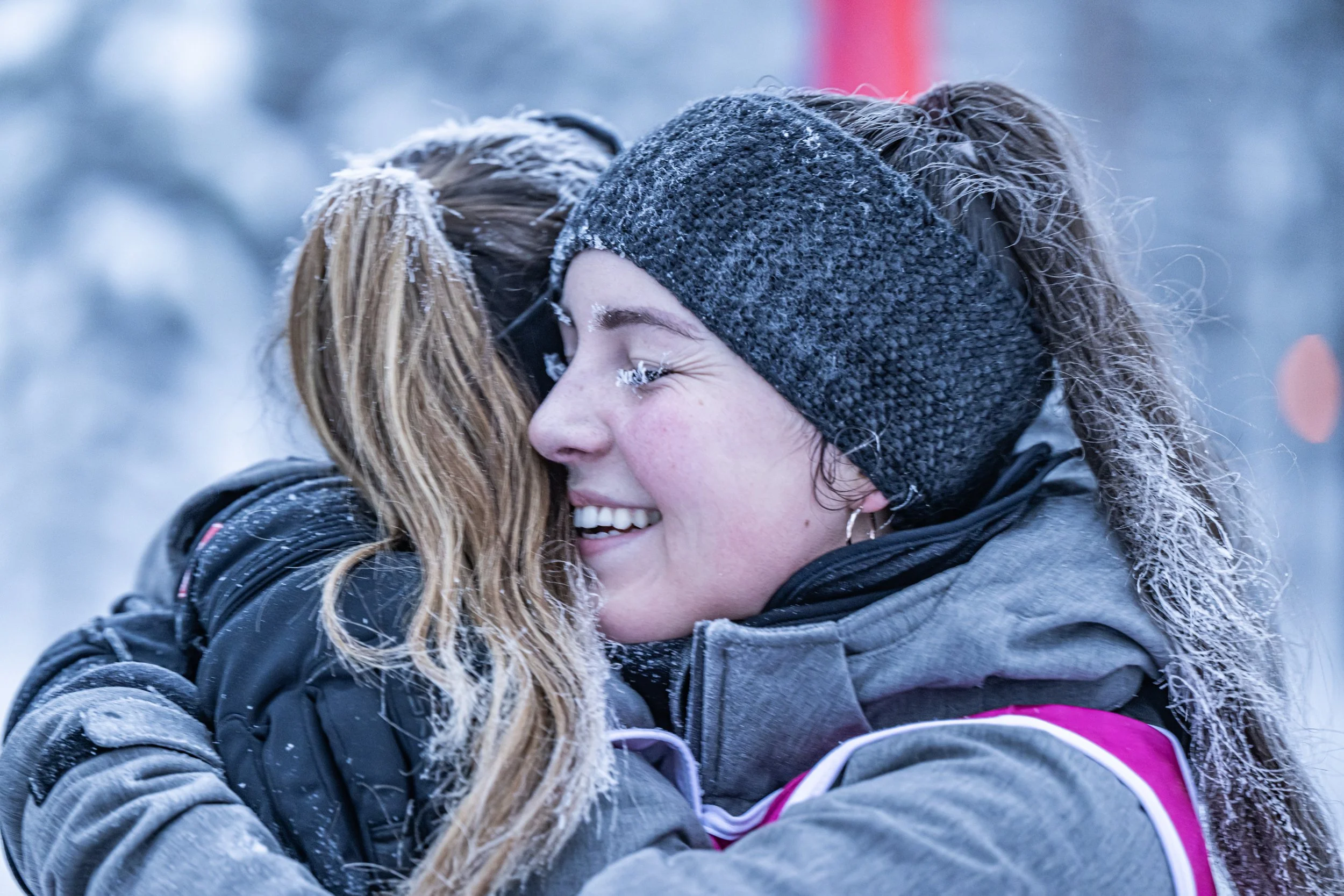 Deux femmes s'embrassent dans un environnement enneigé, portant des vêtements d'hiver.