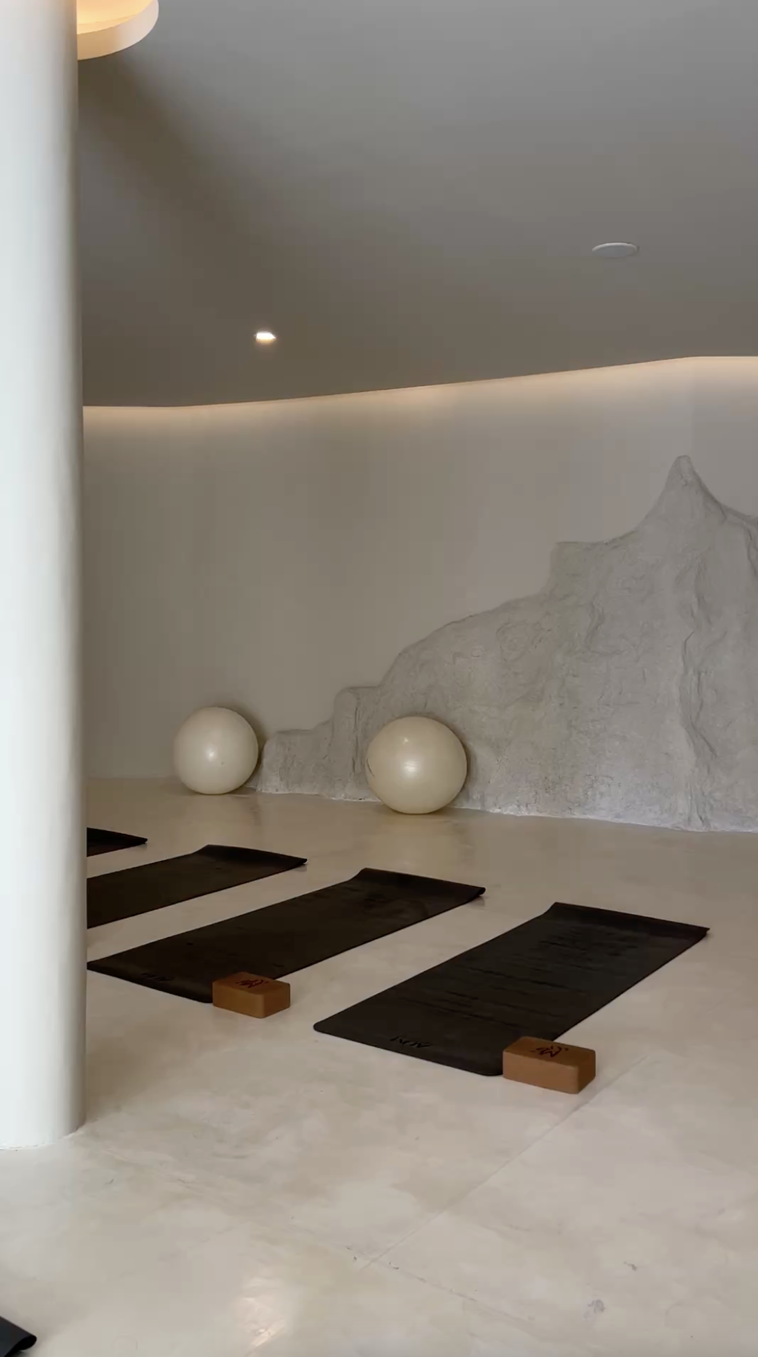 Yoga mats with blocks in a minimalist studio with white walls, spherical props, and a textured mountain mural.