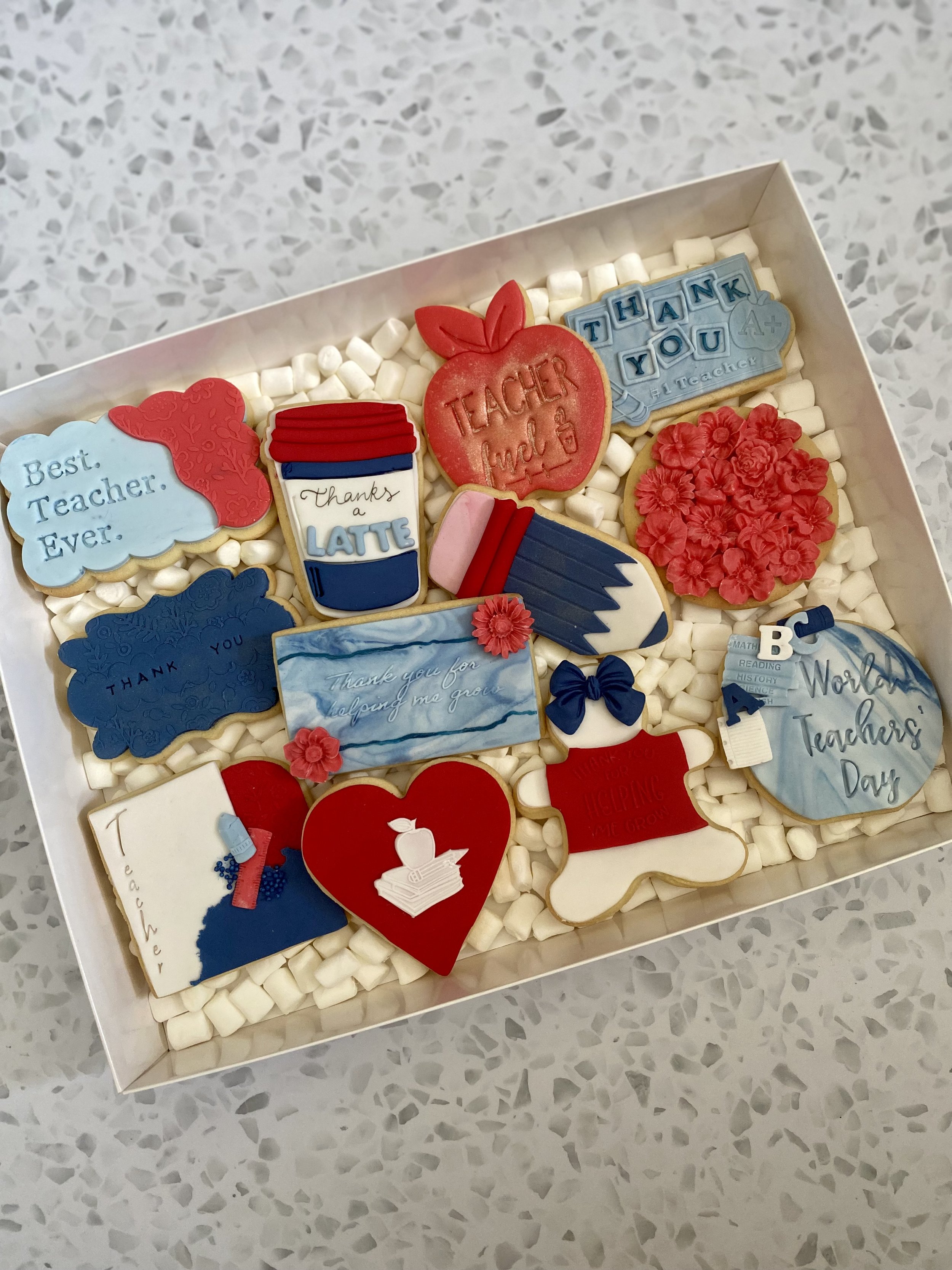 Box of assorted decorated cookies with teacher and thank you themes, including hearts, flowers, a coffee cup, and messages like 'Best Teacher Ever', 'Thank You', and 'World Teacher's Day'.