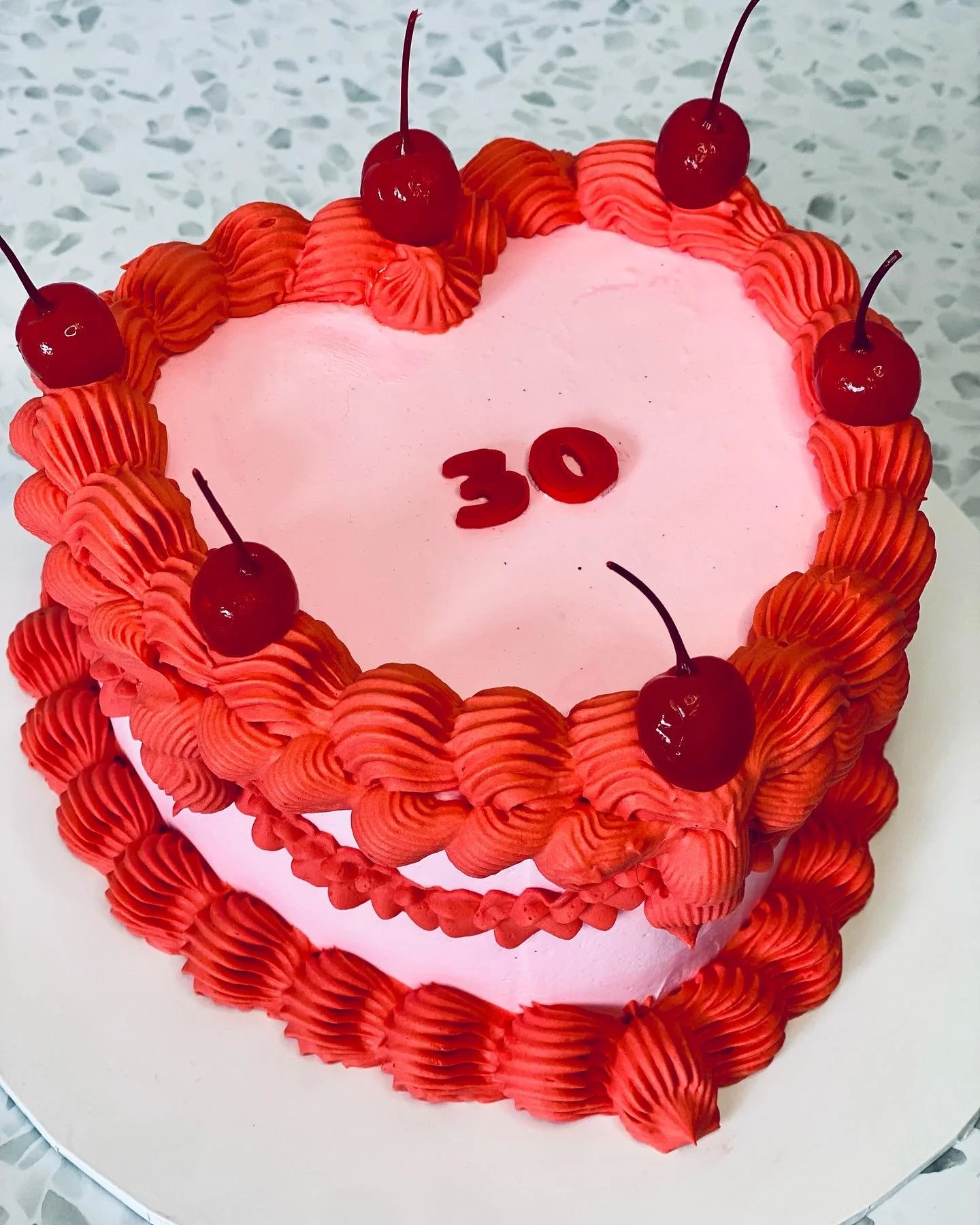 Pink heart-shaped birthday cake with red frosting border and cherries on top, with red 