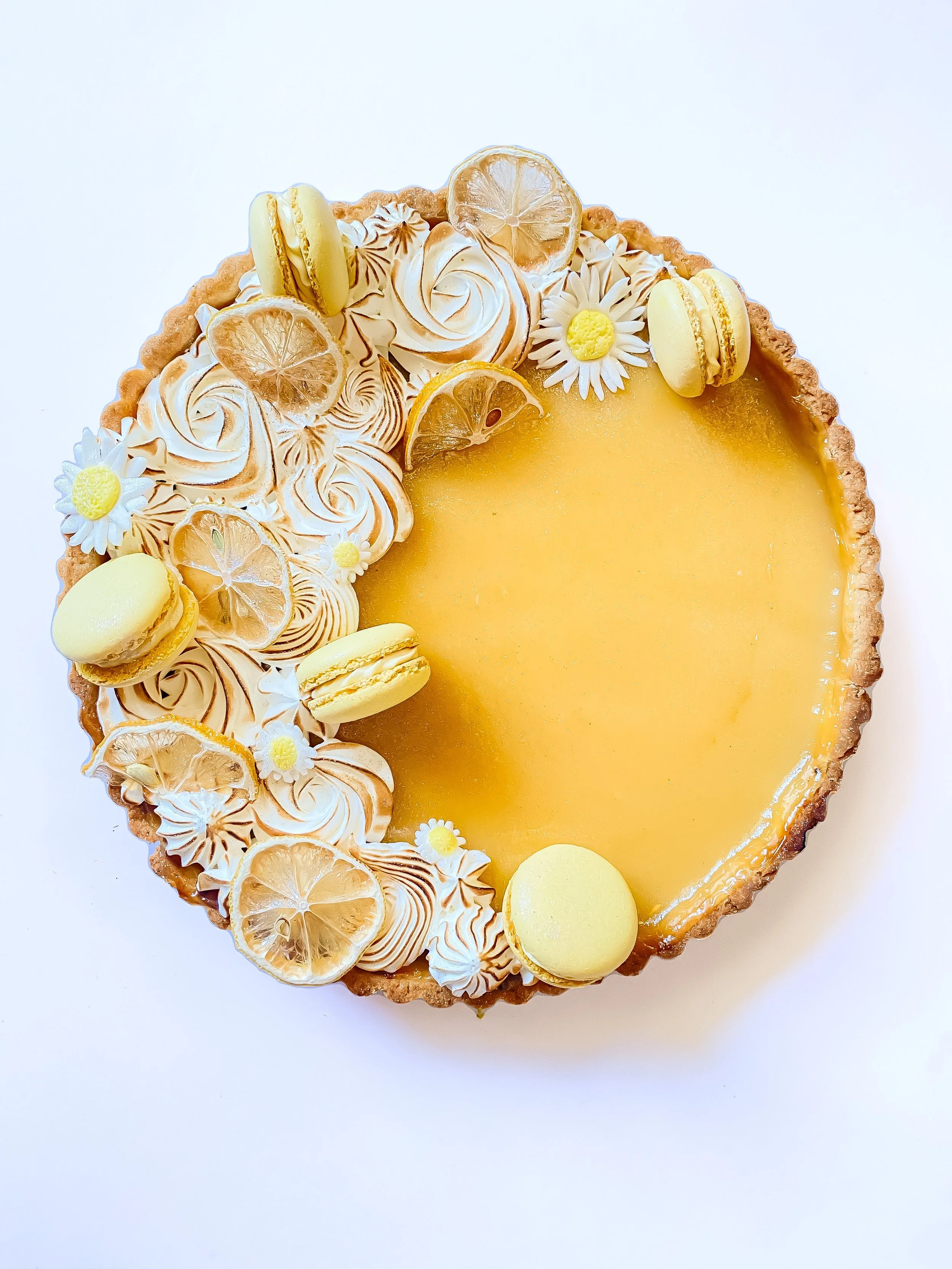 Lemon tart decorated with lemon slices, macarons, and flowers, with one half of lemon slice on top, covered partially in torched meringue swirls