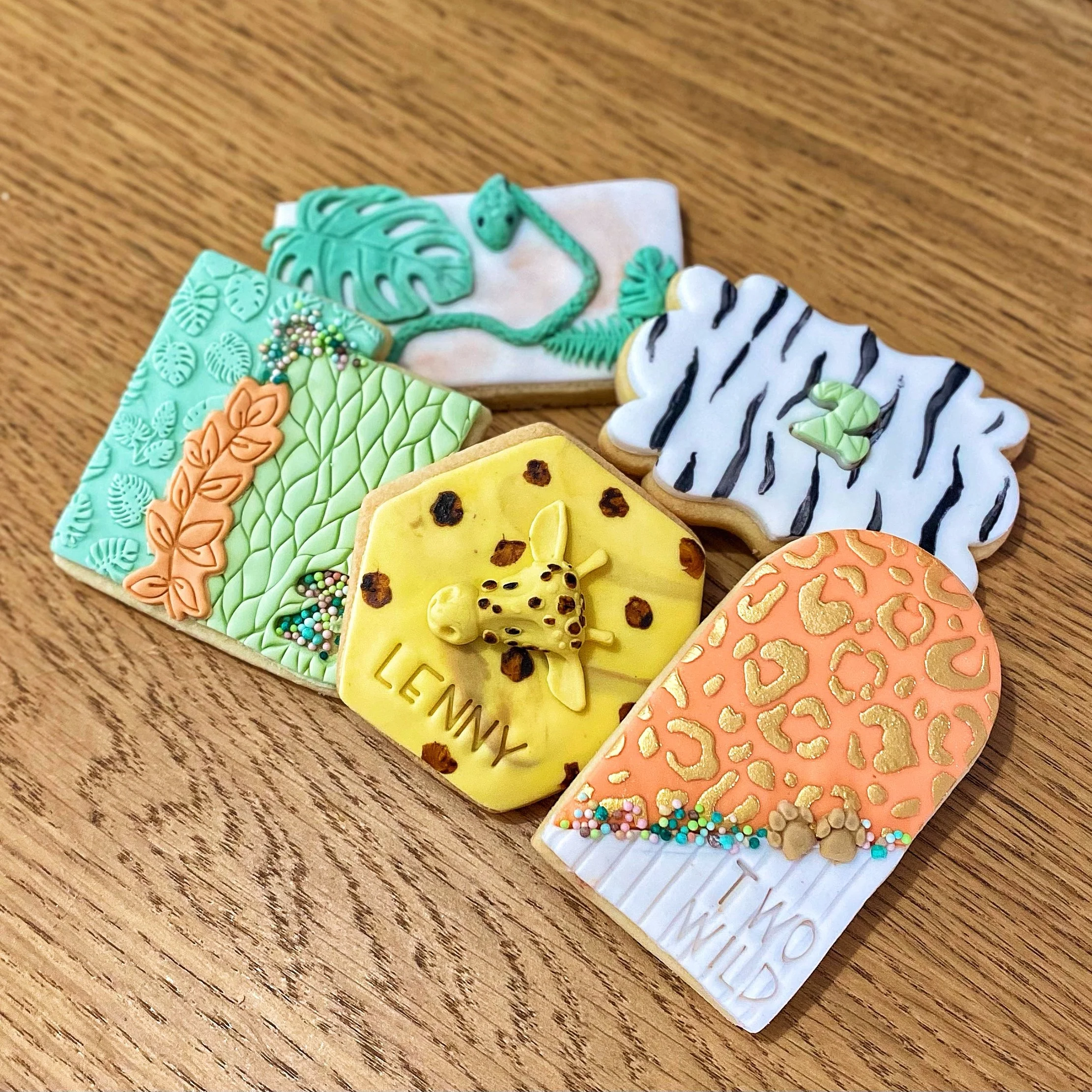 Decorated animal print cookies with jungle and animal themes, featuring designs of leaves, a zebra pattern, a giraffe, and a leopard print, arranged on a wooden surface.
