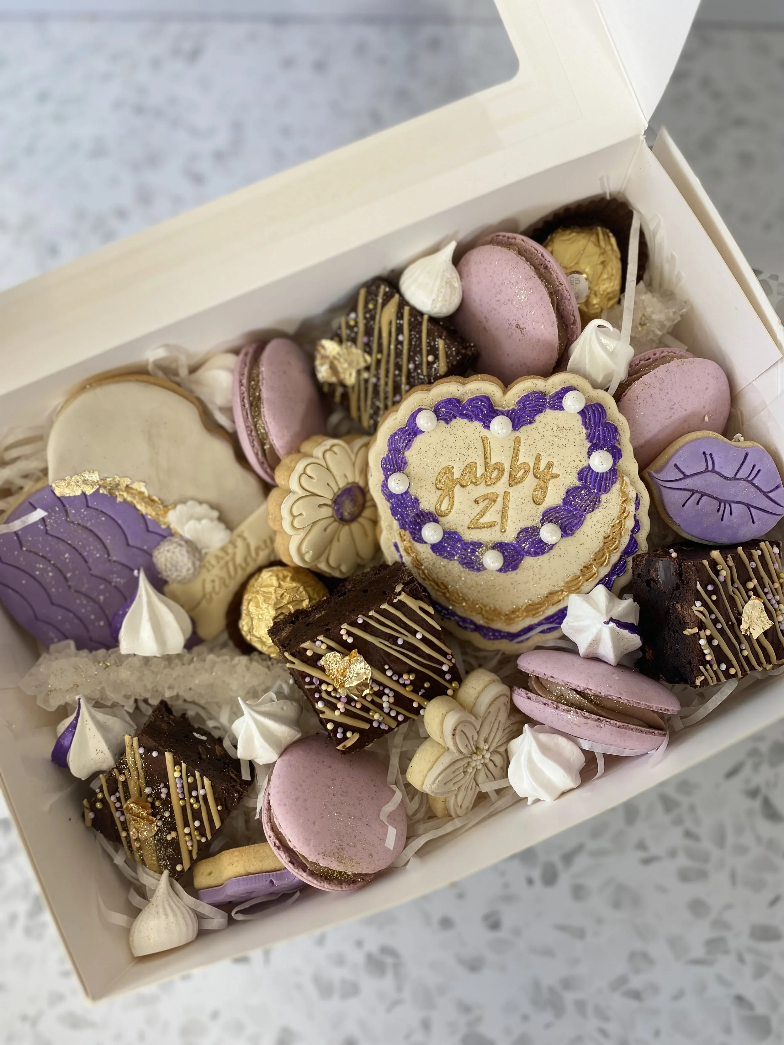 Decorated cookies and chocolates in a box with a message 'gabby 21'.