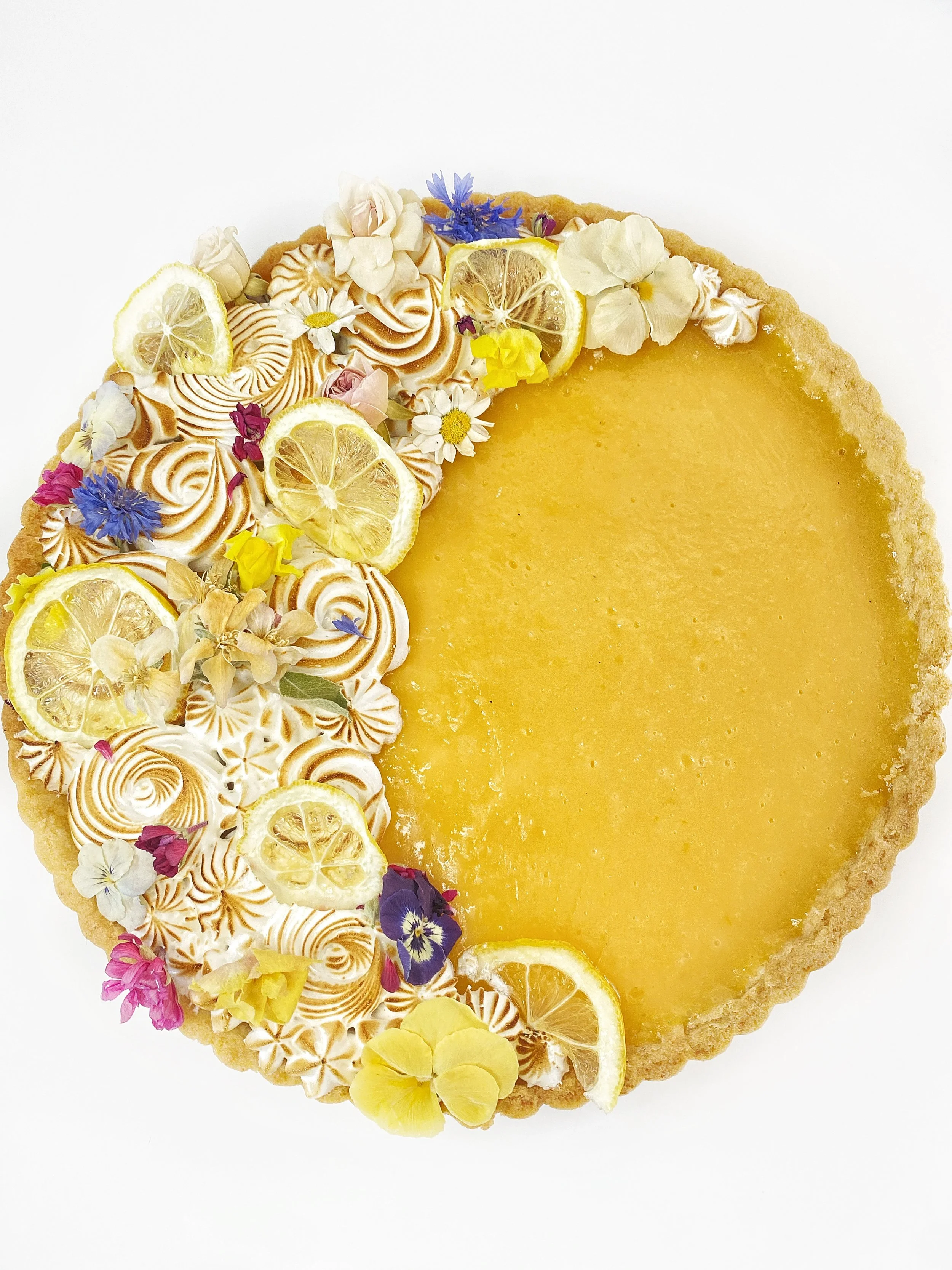 Lemon tart decorated with lemon slices and colorful edible flowers on a white background.