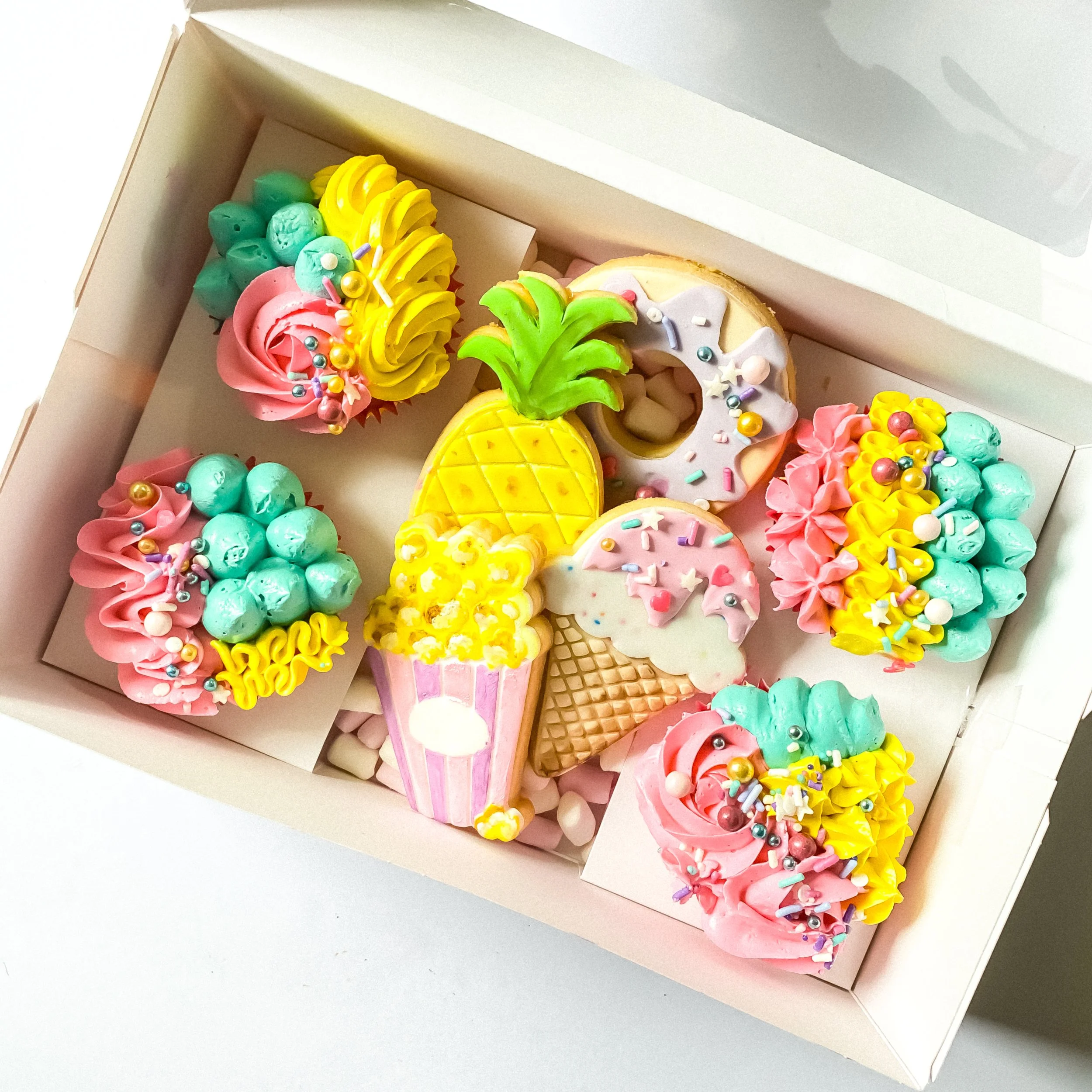Colorful clay or fondant cupcakes and ice cream cone decorations inside a white box.