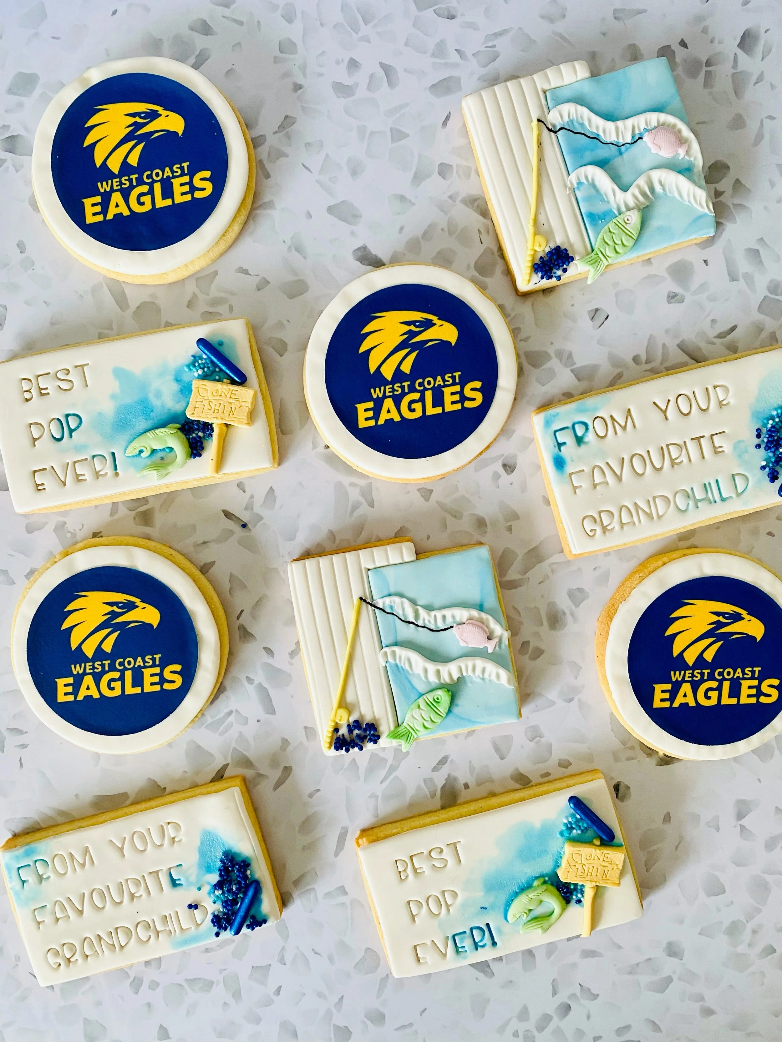 Decorative cookies with West Coast Eagles logo, fishing theme, and messages like "Best Pop Ever!" and "From Your Favourite Grandchild" on a white speckled surface.