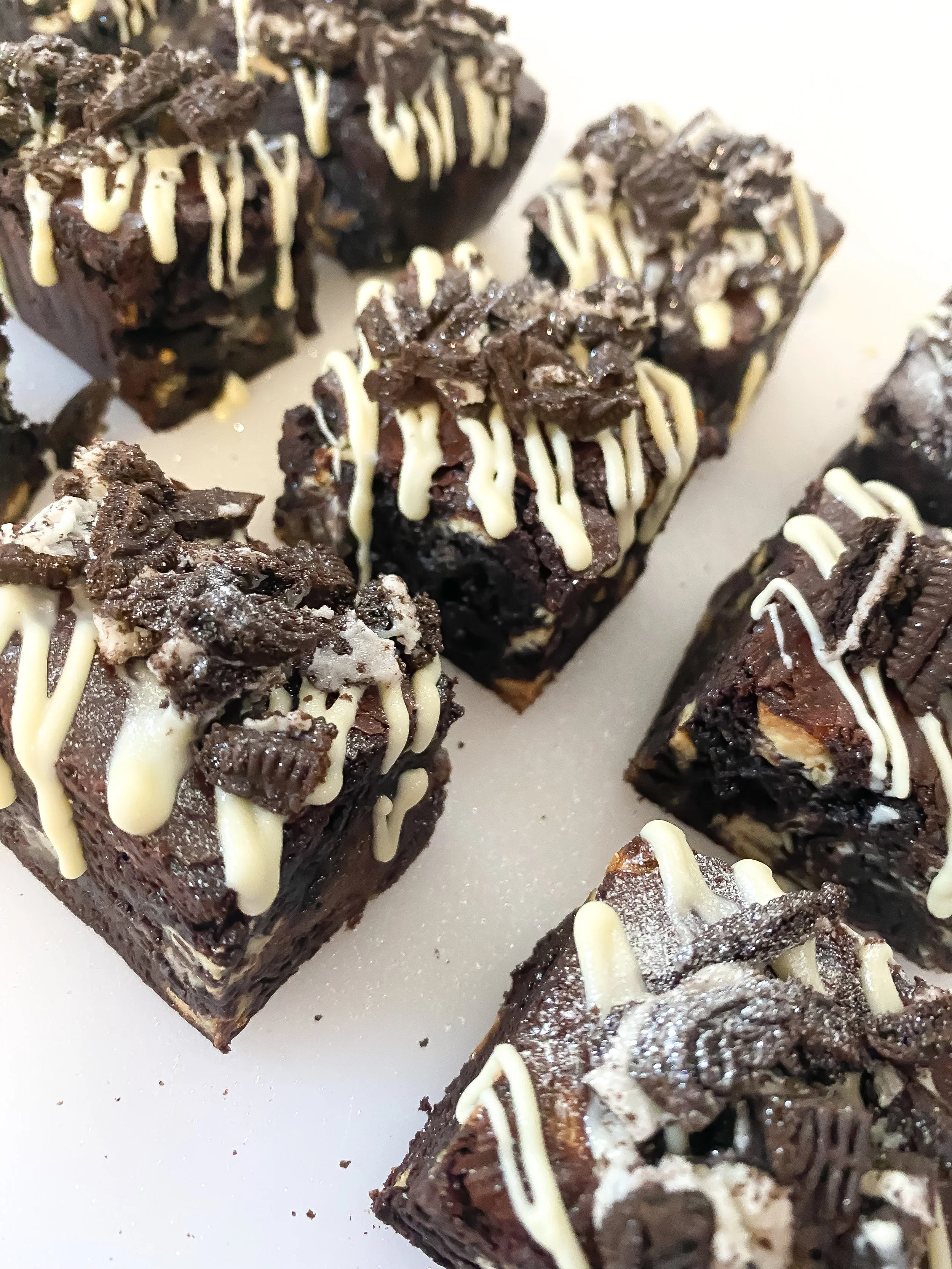 Close-up of chocolate brownie squares topped with crushed cookies, drizzled with white chocolate.