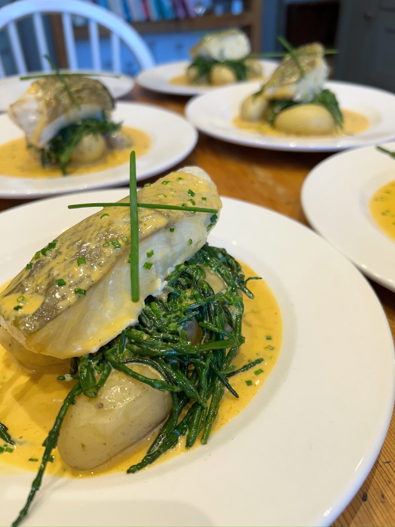 Plates of poached eggs on a bed of greens with hollandaise sauce, garnished with chives, served on white plates.
