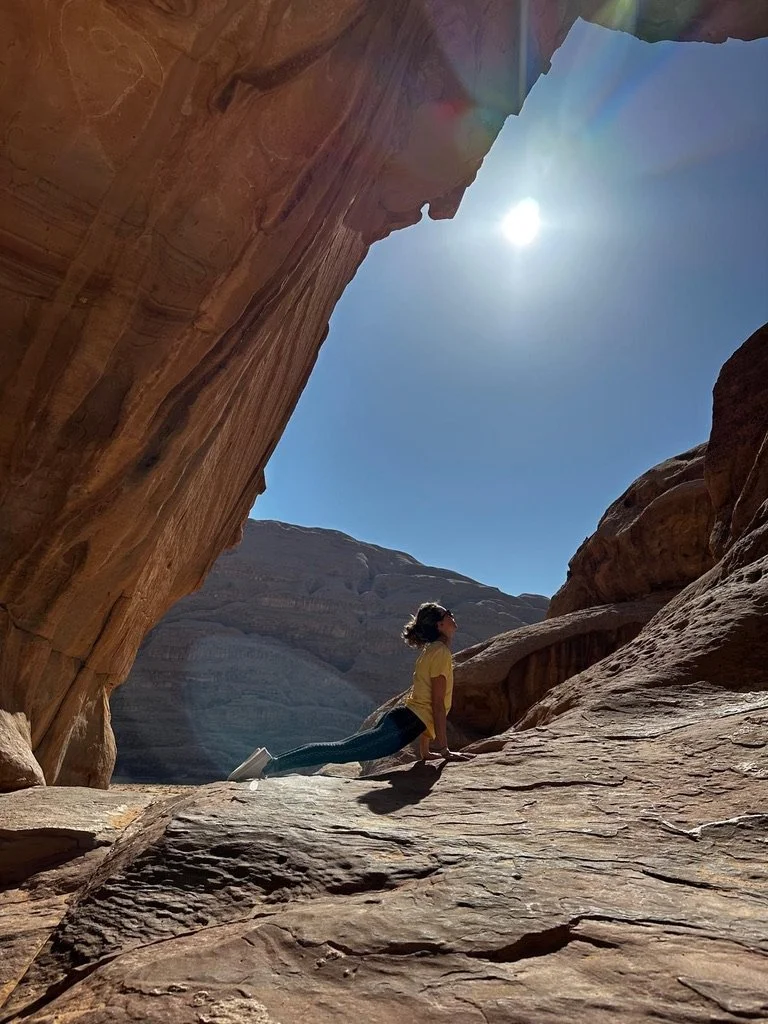 Une femme faisant du yoga ou de l'exercice en position de planche sur une roche dans un canyon rocheux, avec le soleil brillant dans un ciel clair.