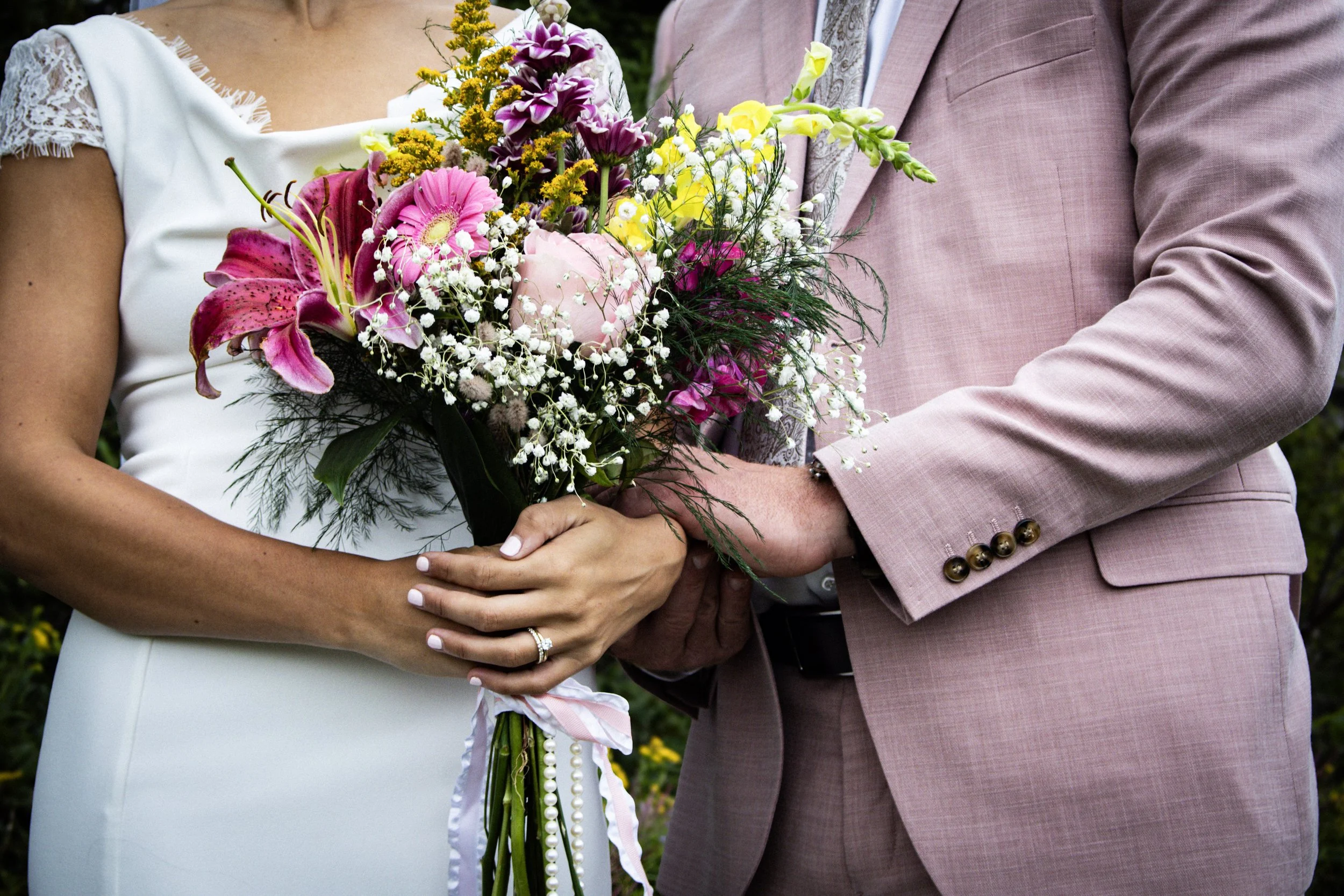 Close-up of a bride and groom holding a bouquet of colorful flowers during a wedding