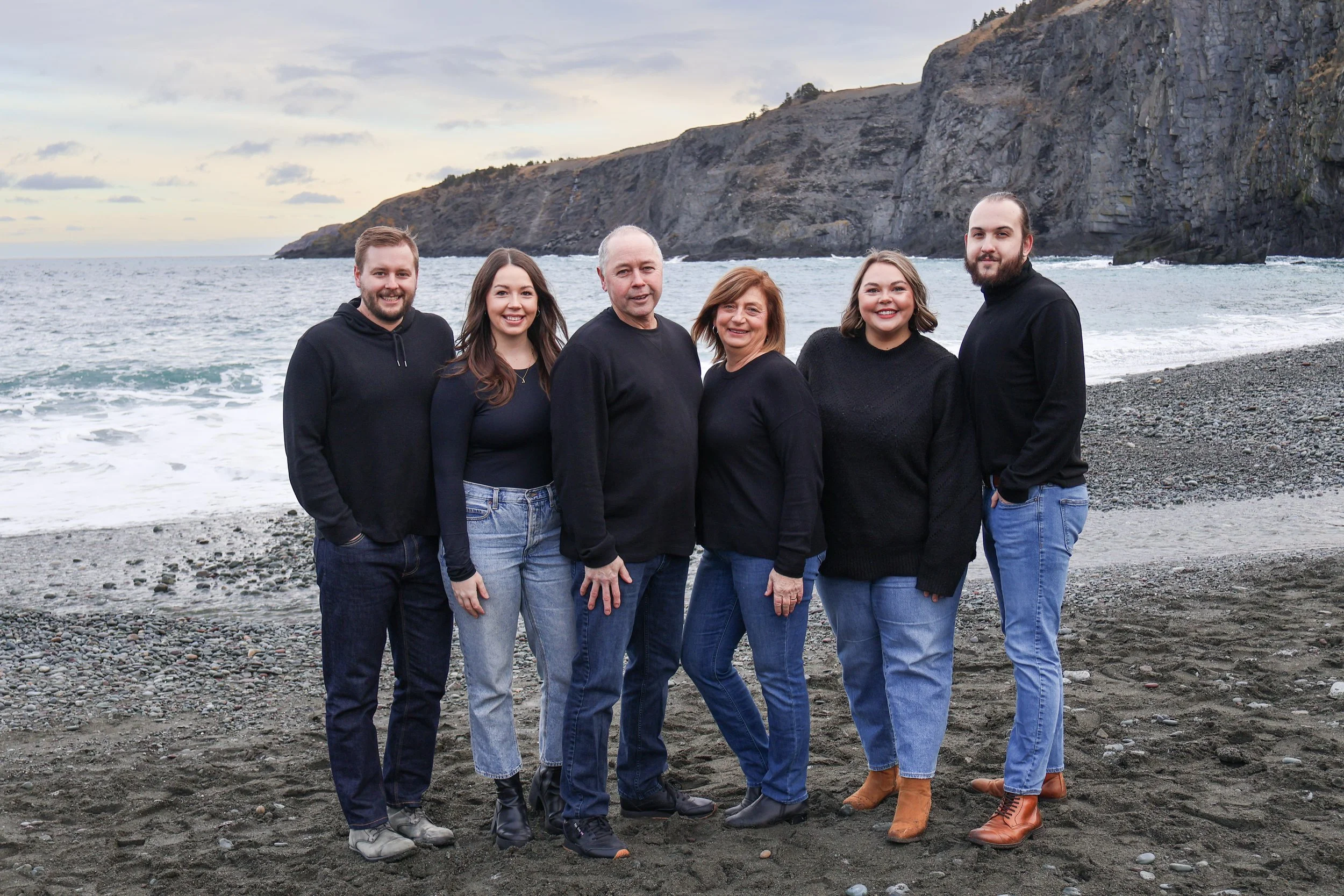 Family of six standing on a beach with cliffs and the ocean in the background