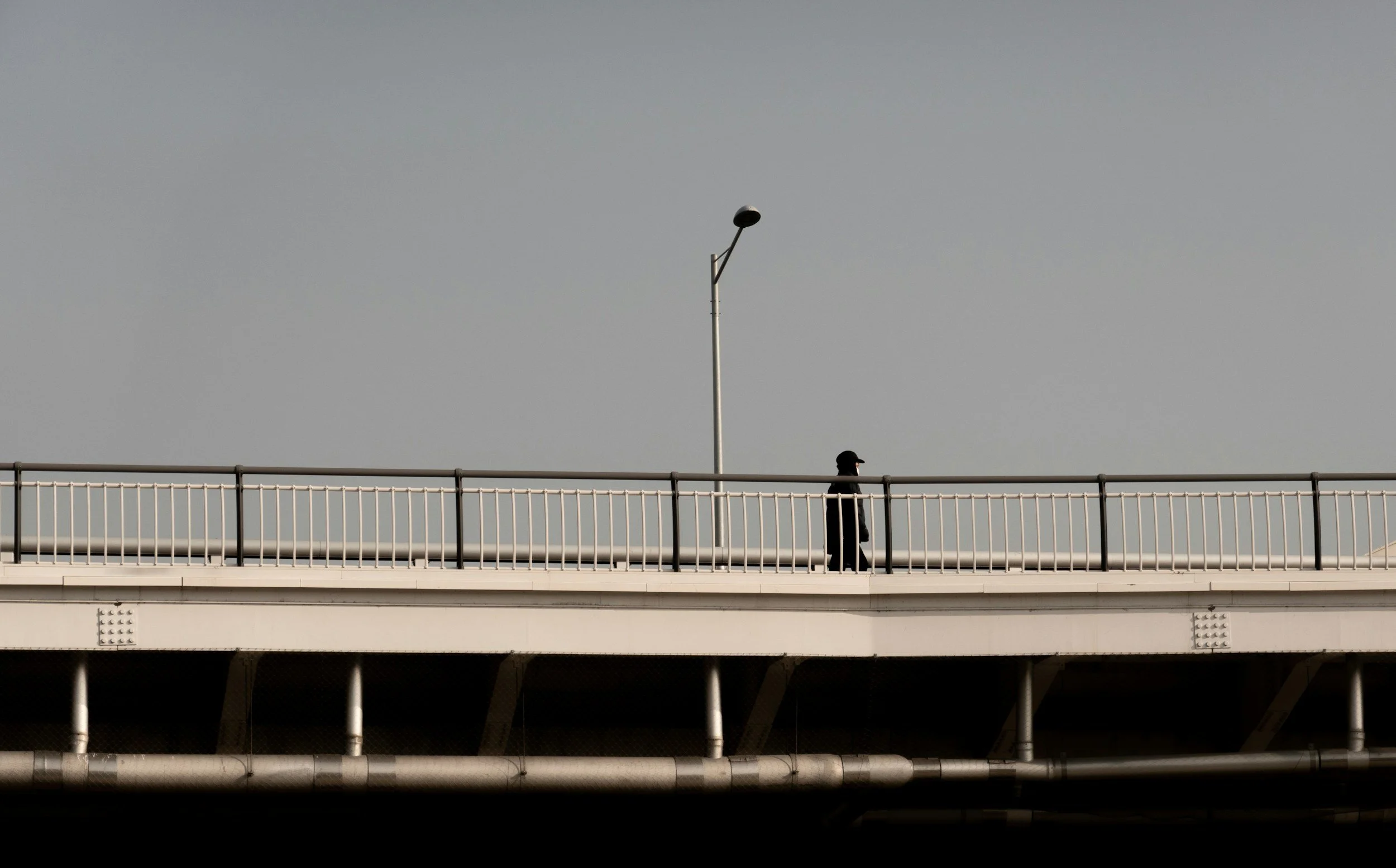 Ein Mensch geht auf einer Brücke, mit einer Straßenlaterne und einem klaren Himmel im Hintergrund.