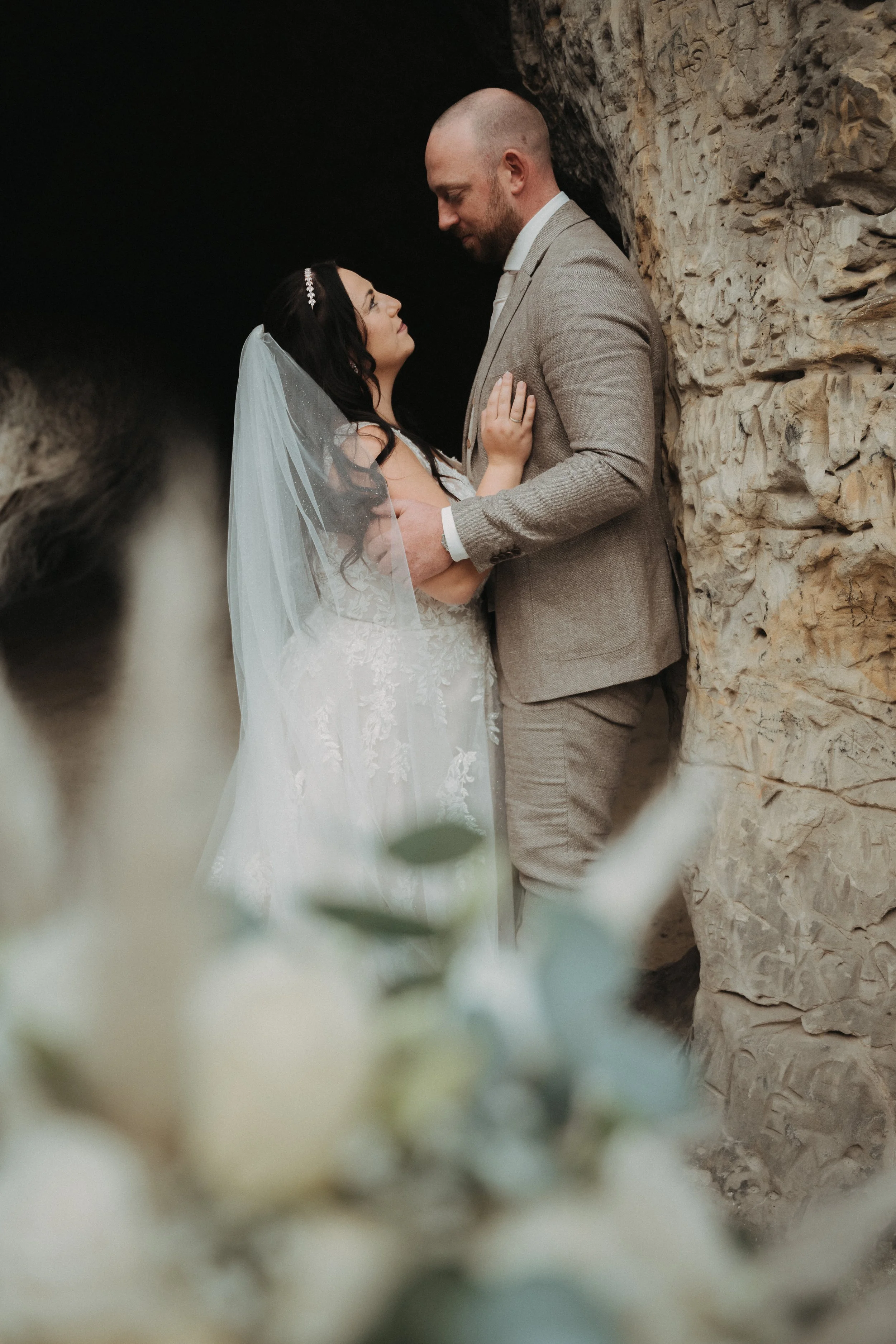 Ein Brautpaar steht sich in einer Felsengrotte gegenüber, hält sich an den Händen und blickt sich liebevoll an.