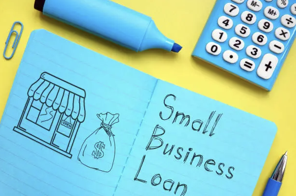 Open notebook with a drawing of a small business storefront, a bag with a dollar sign, and the words "Small Business Loan" written on the pages.