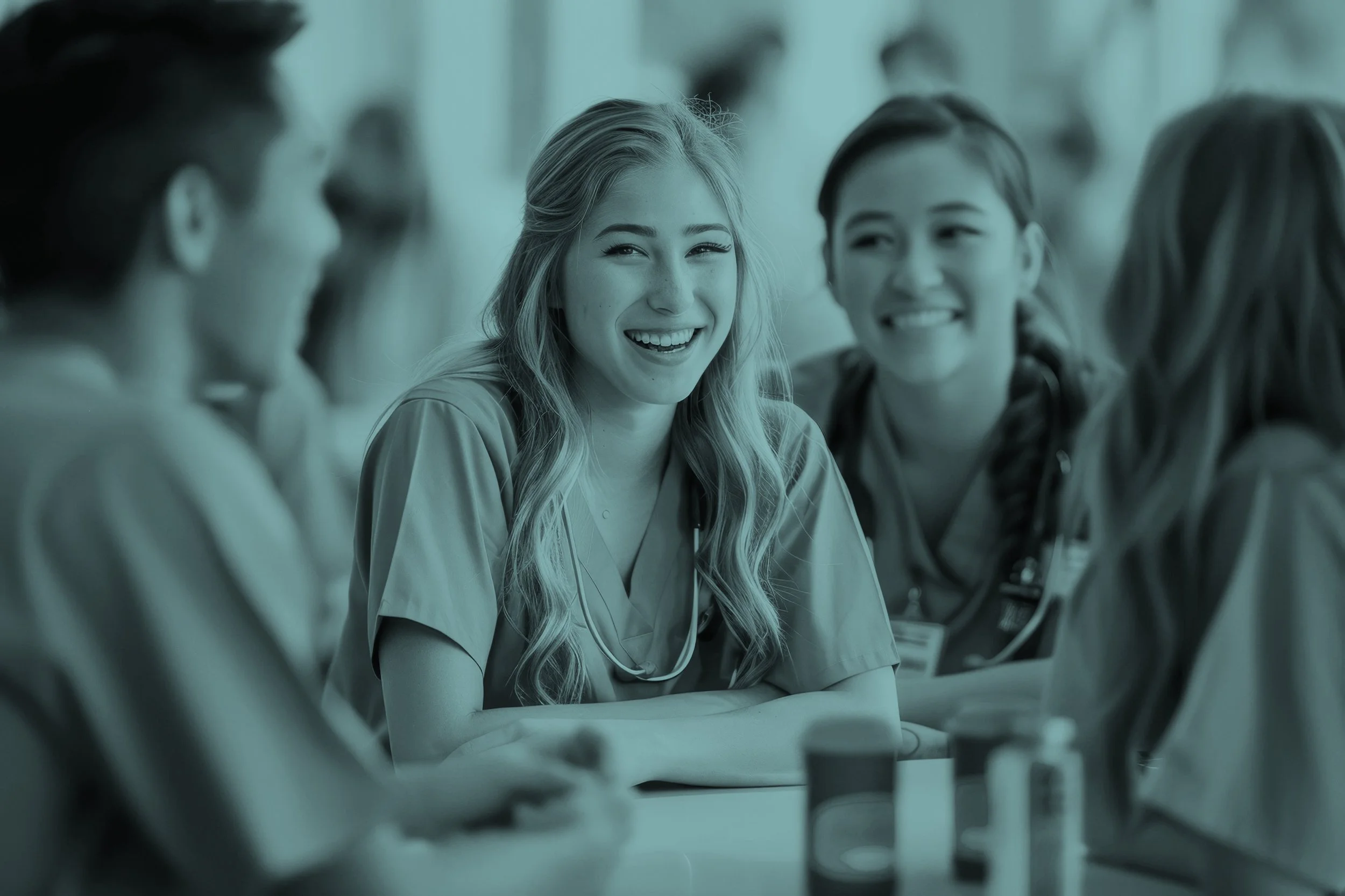 Group of healthcare professionals in scrubs sitting at a table and laughing together.