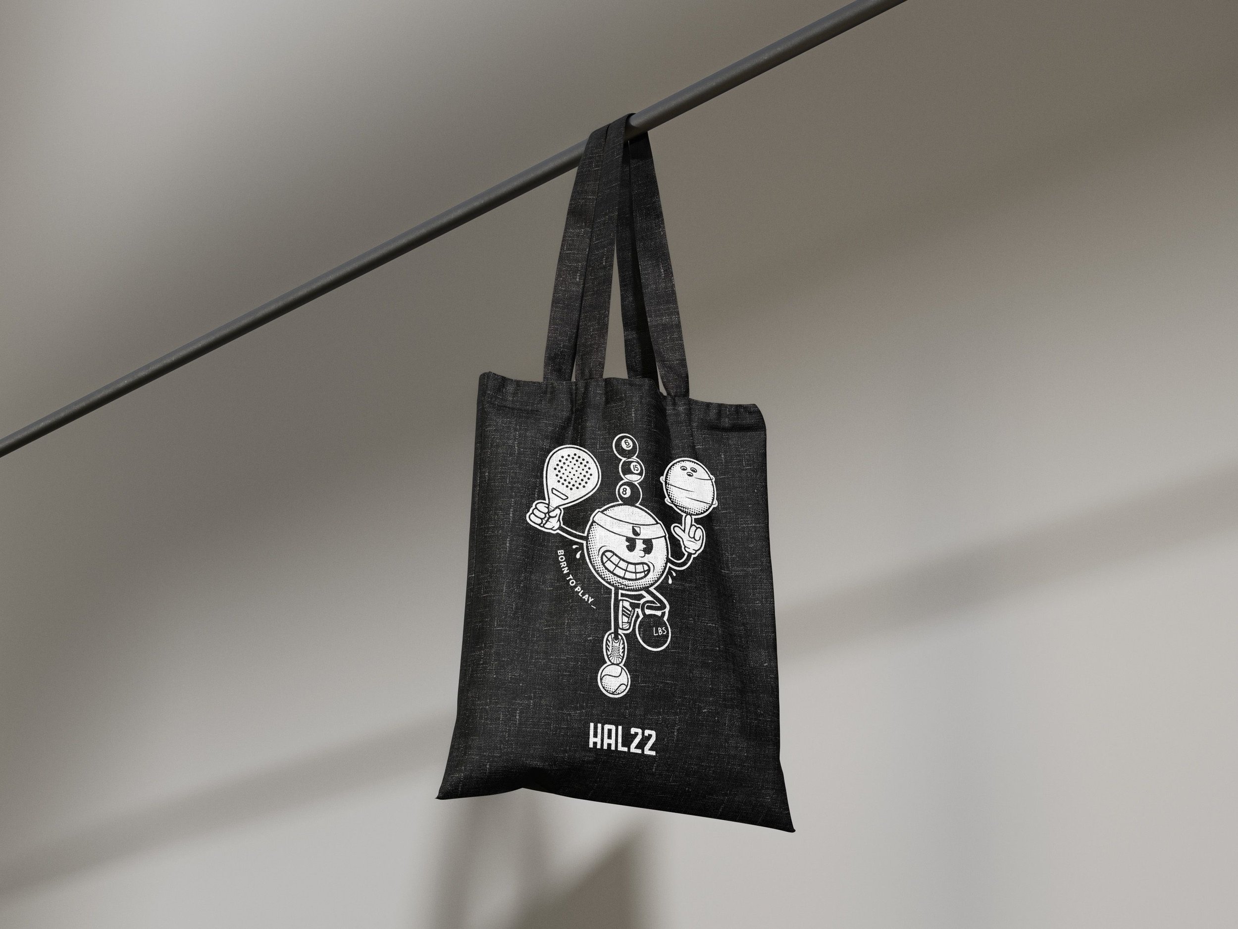 A black tote bag hanging from a horizontal rod, featuring a cartoon character playing tennis and holding a tennis ball, with the text "HAL22" at the bottom.