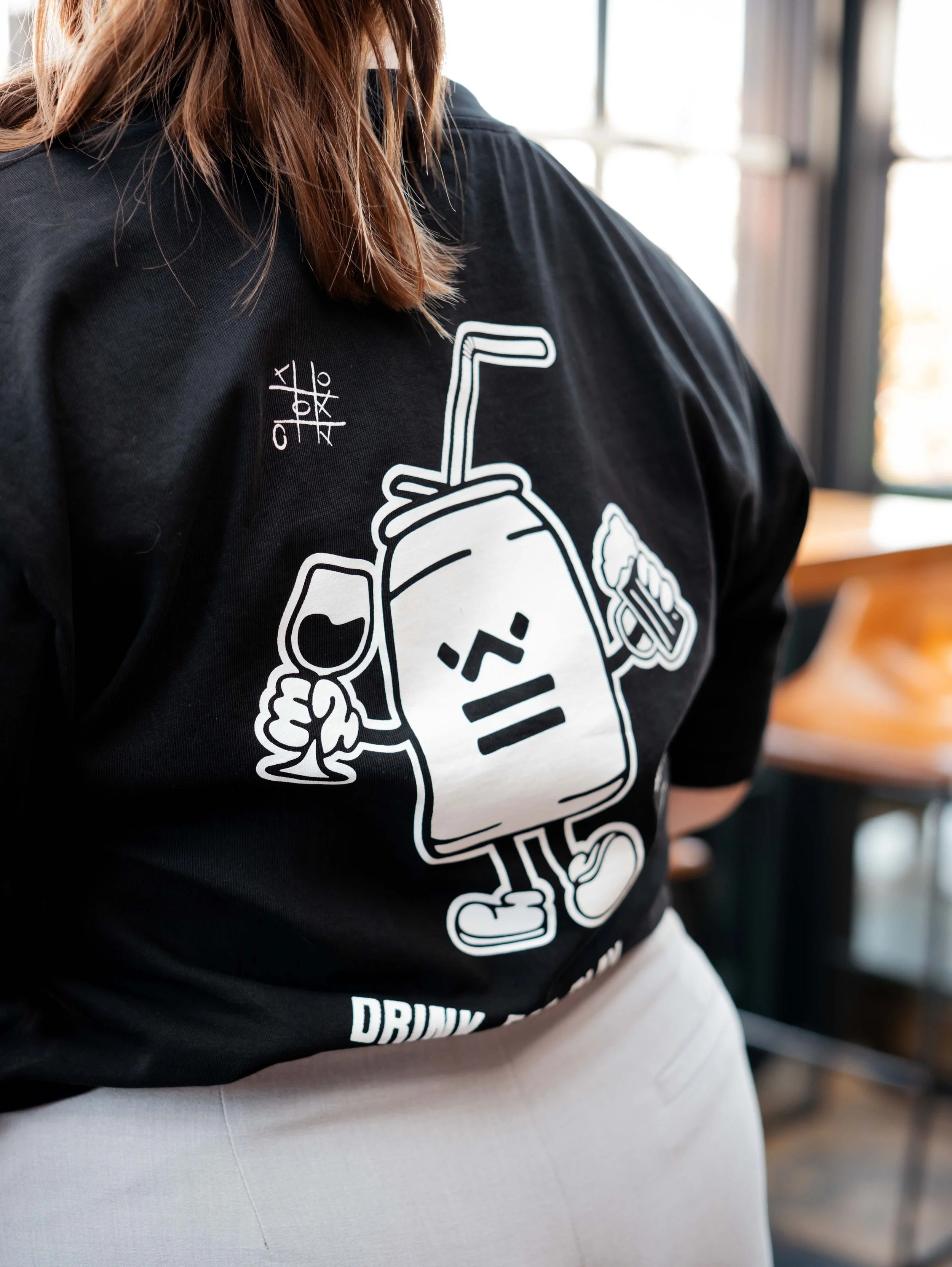 Person wearing a black t-shirt with a cartoon drink character holding a wine glass and a beer mug.