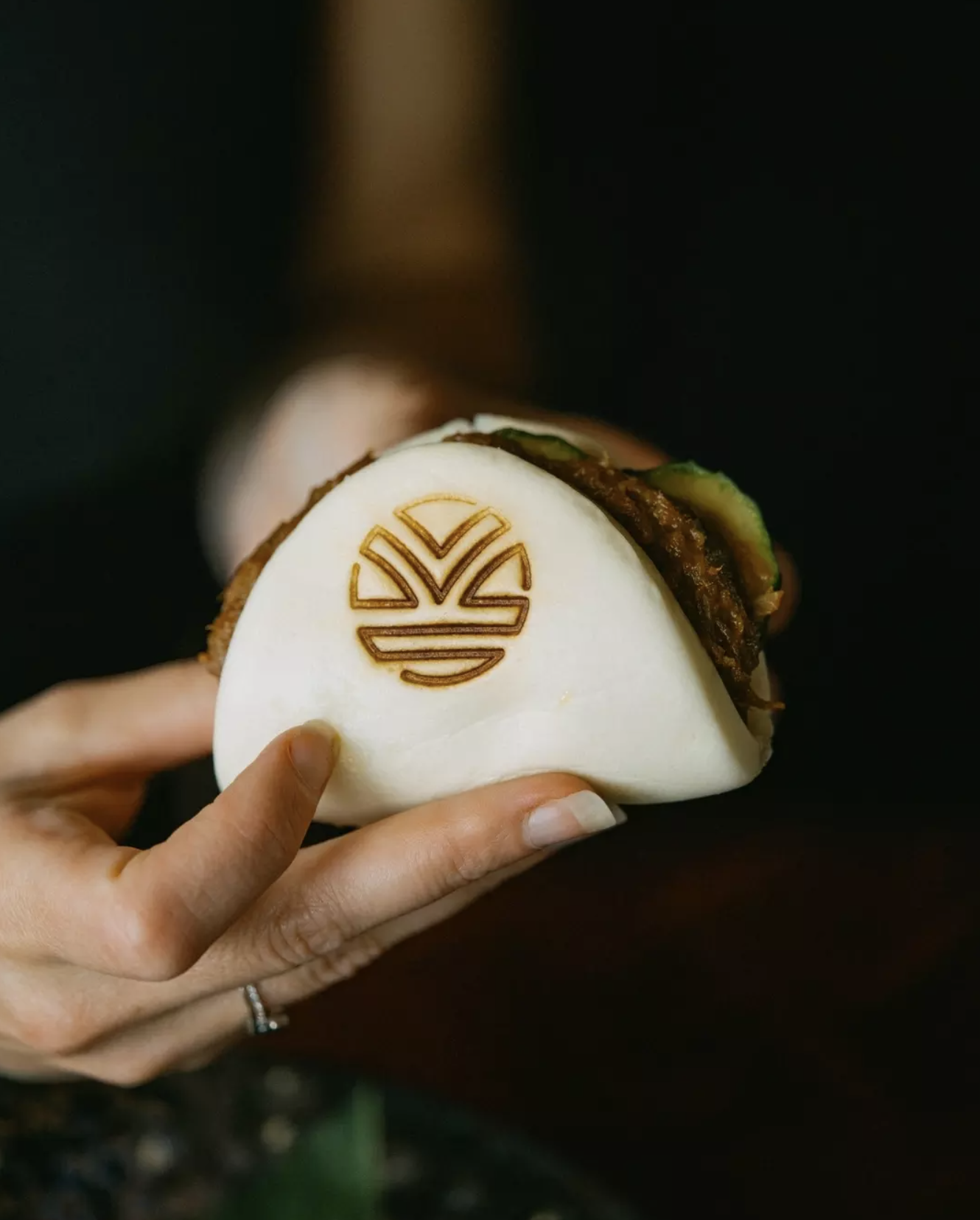 A hand holding a bao bun with a printed logo on the bun.