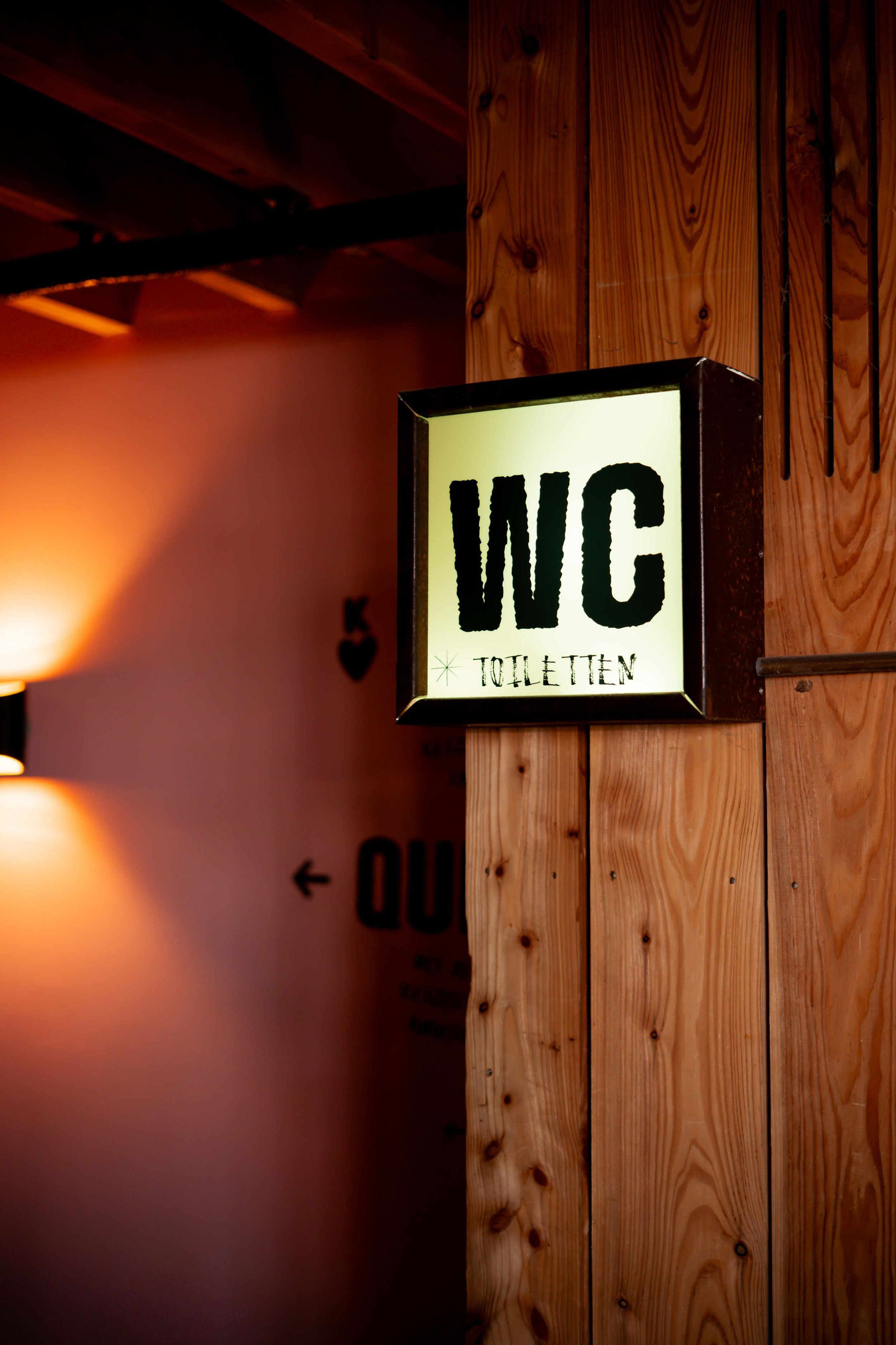 Illuminated sign reading "WC Toiletten" on wooden wall in indoor setting.