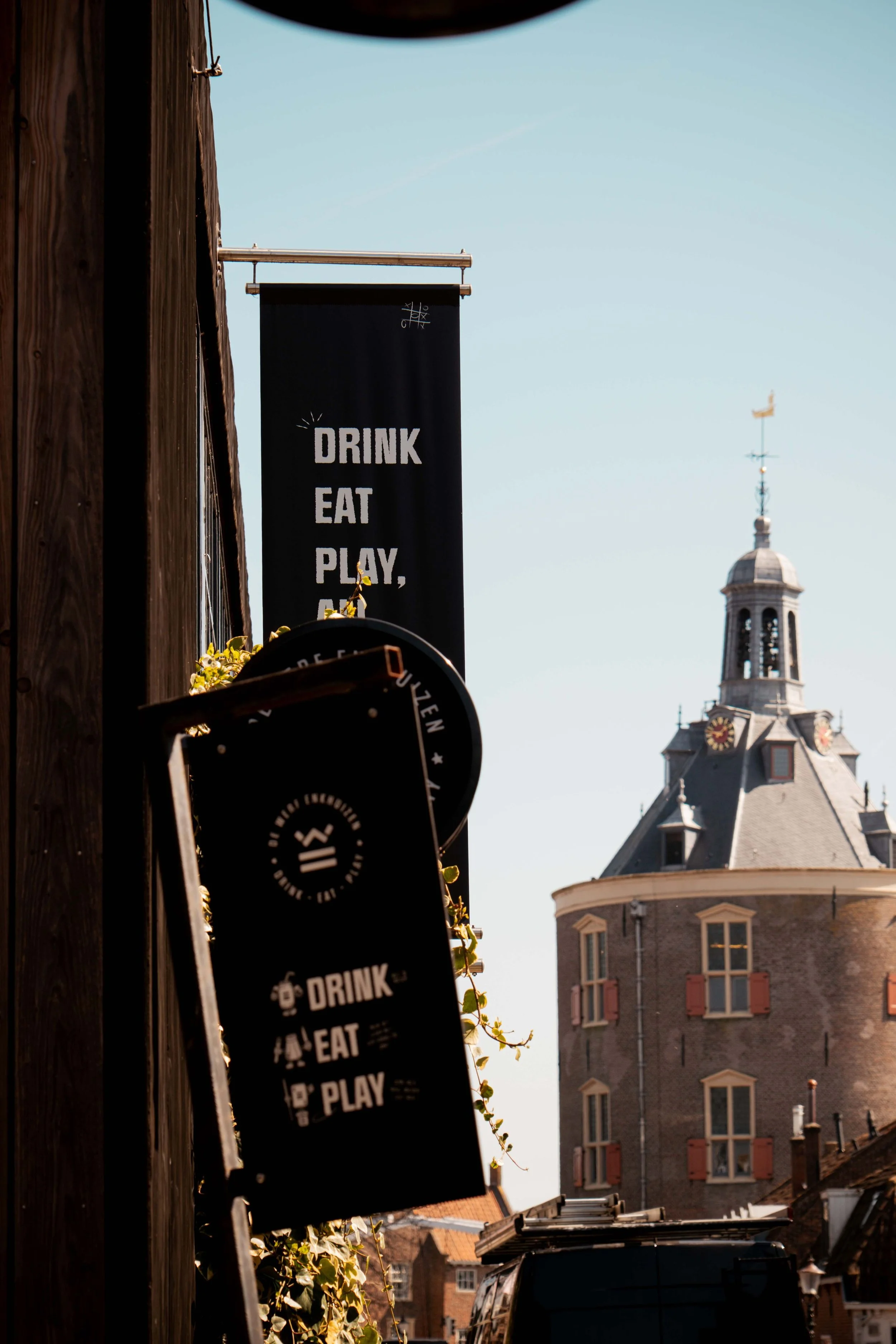 Street scene with signs displaying 'Drink, Eat, Play' and a historic clock tower in the background.