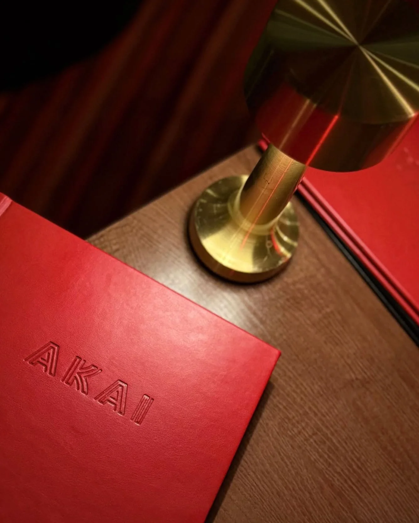 A red Akai box, a gold table lamp with a black lampshade, and a wooden surface with a dark background.