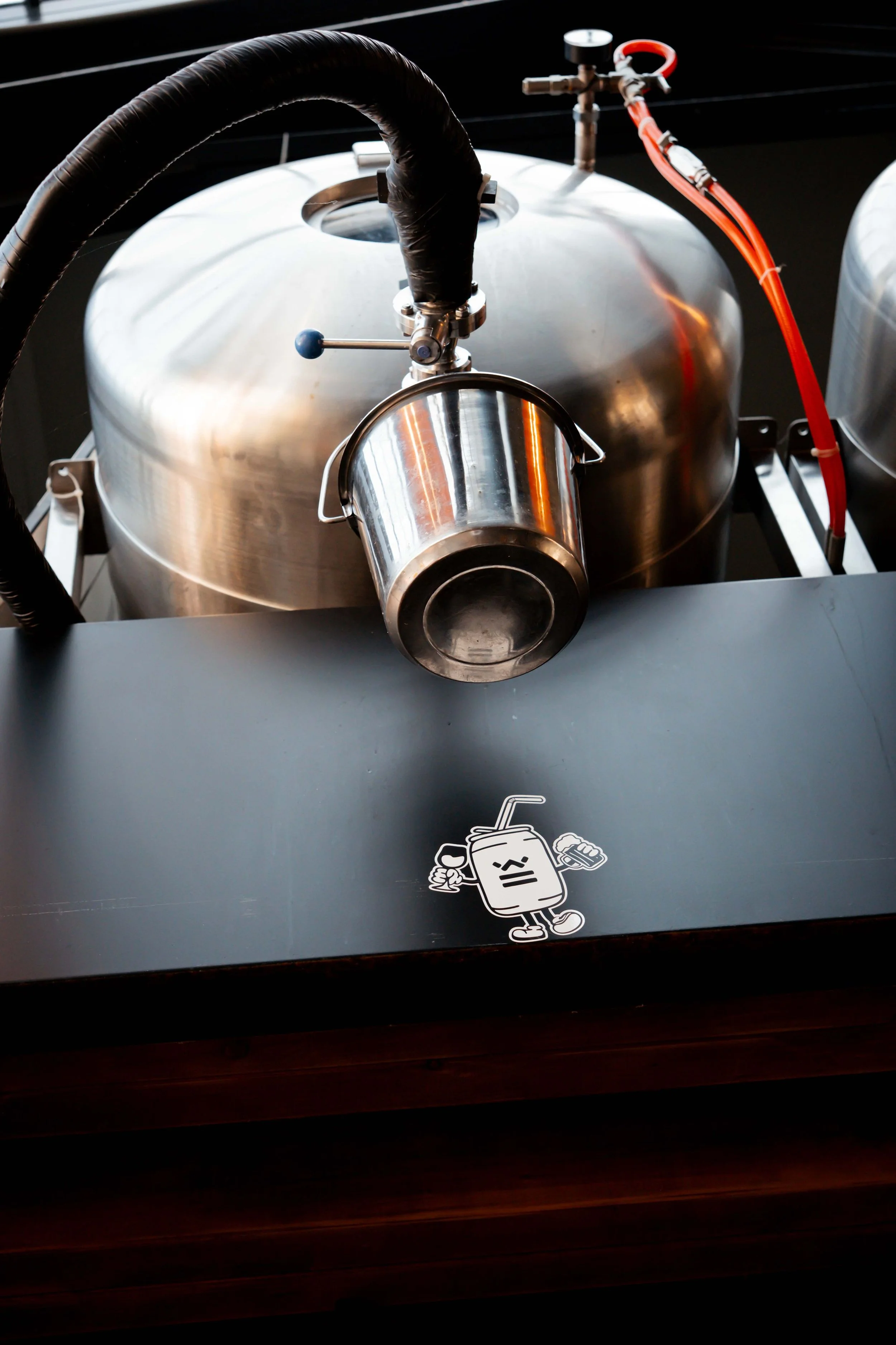 Close-up of a commercial coffee roasting machine with a cartoon sticker of a happy coffee cup on the black surface in front.