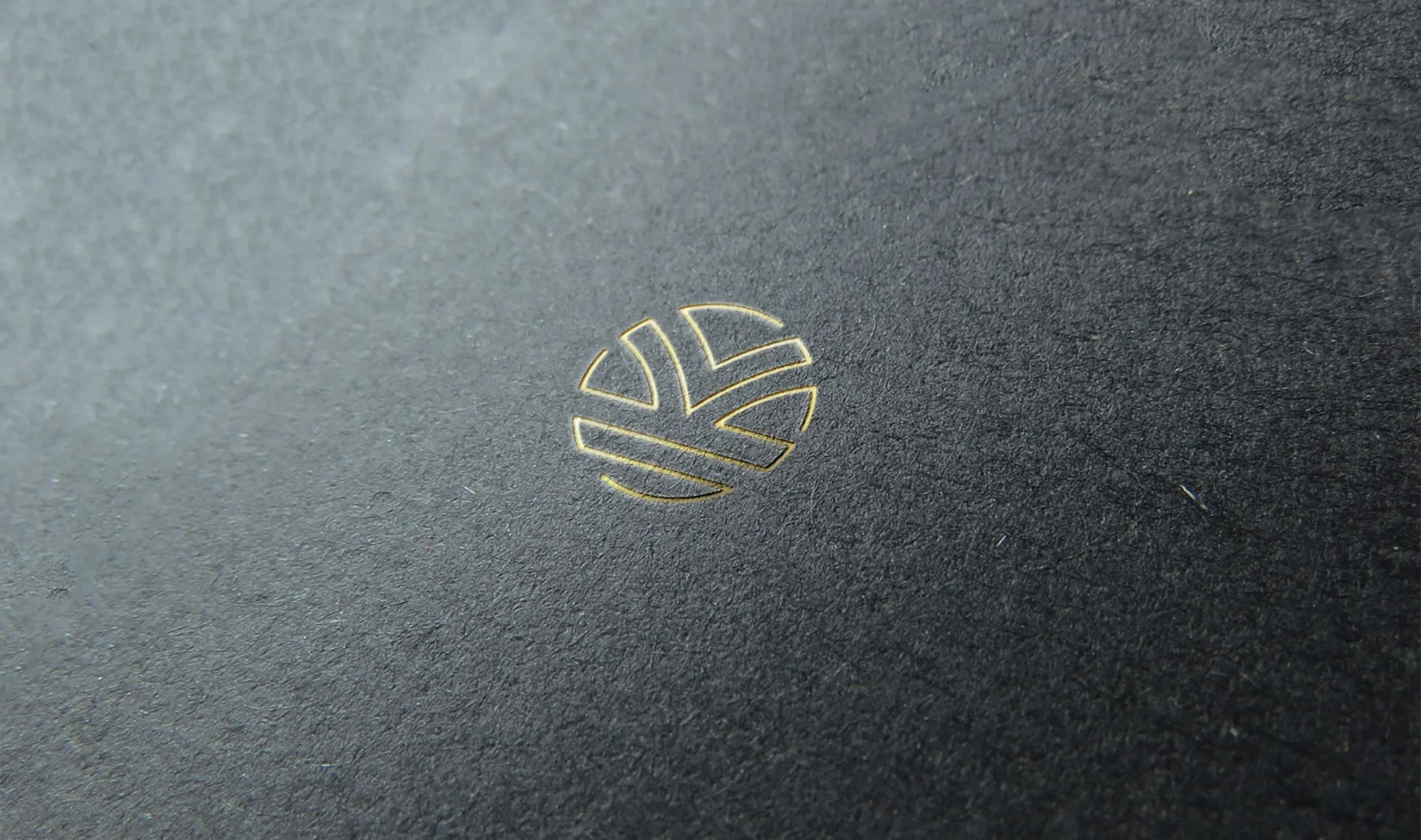 Close-up of a black textured surface with a small, gold geometric icon resembling a stylized globe or seal at the center.