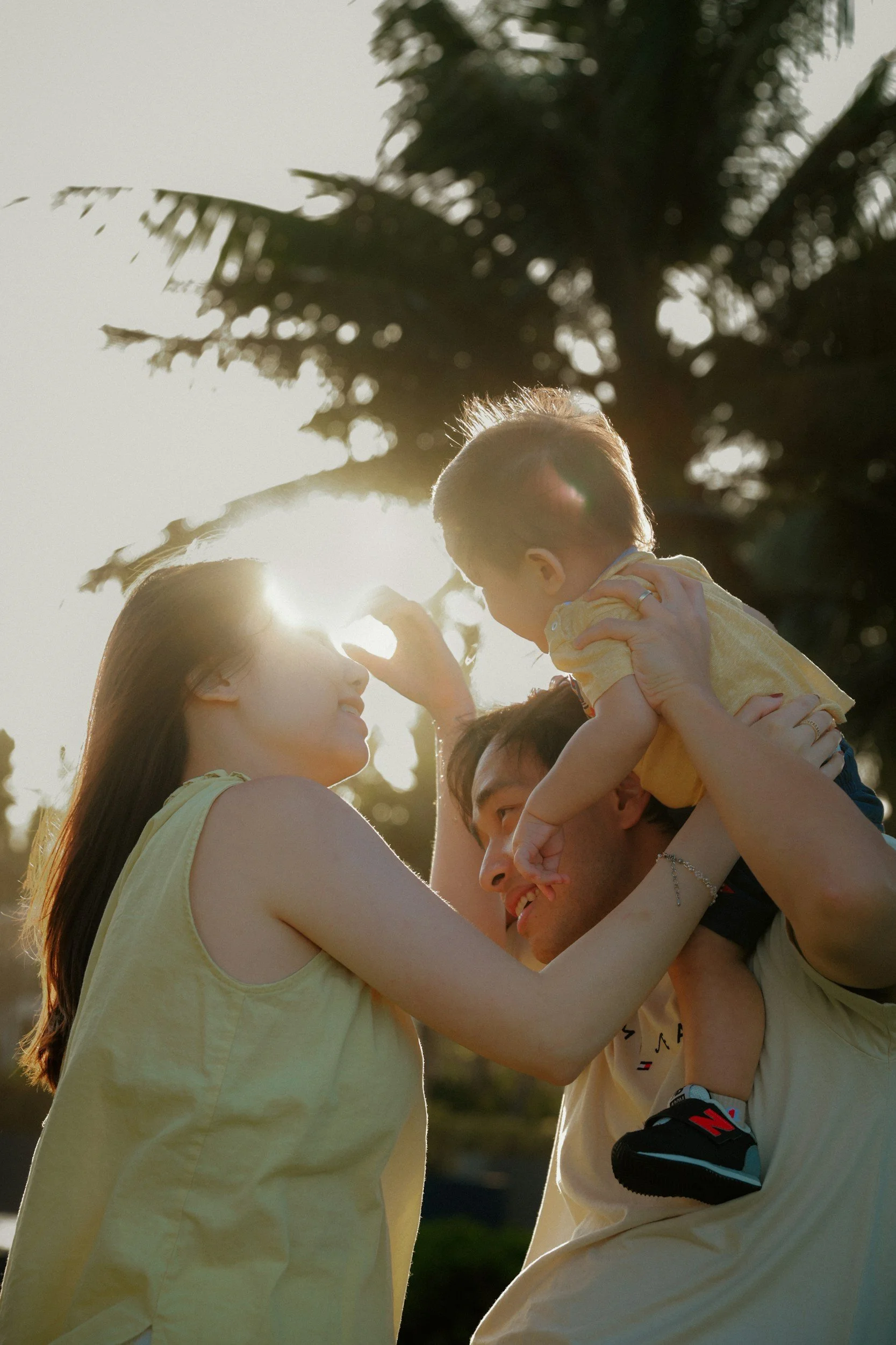 A family of three enjoying time outdoors during sunset, with the mother and father holding their young son who is reaching towards the mother.