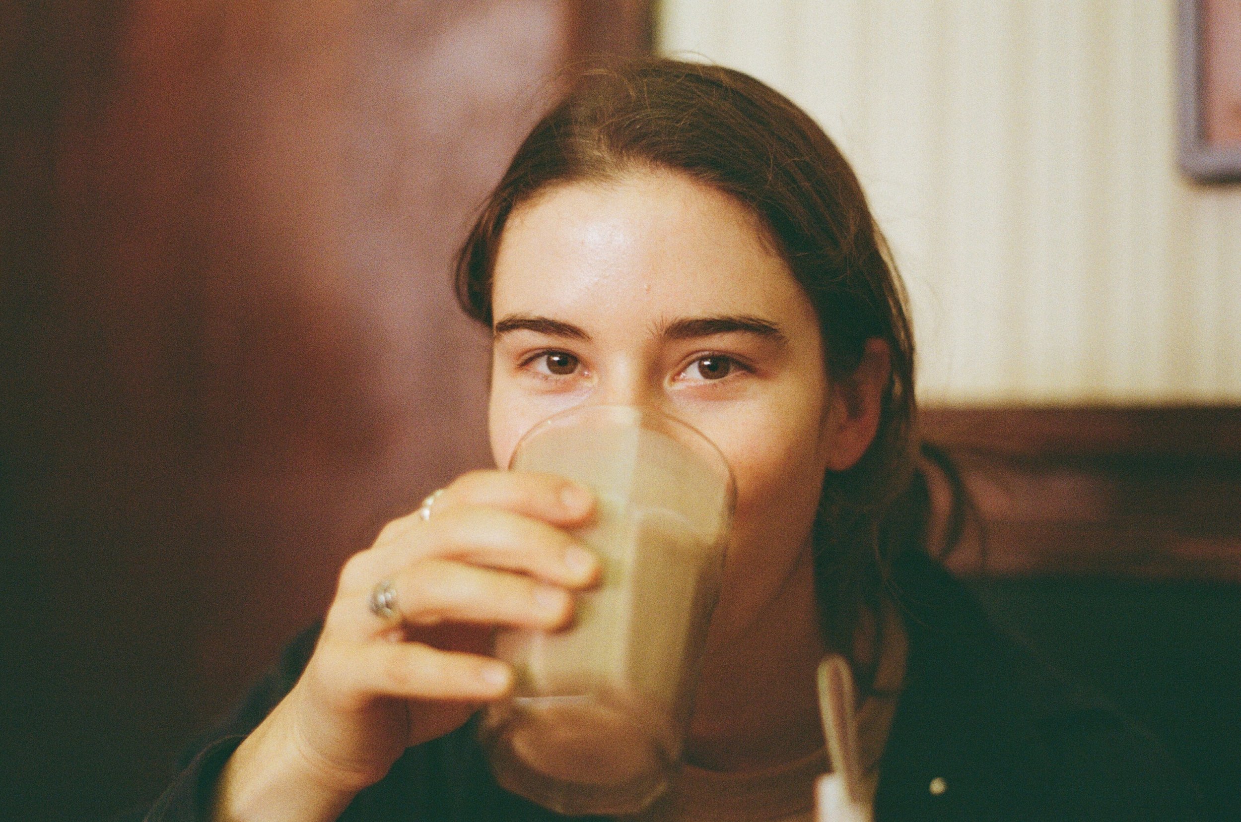 A young woman with brown hair drinking a smoothie or milkshake from a glass.