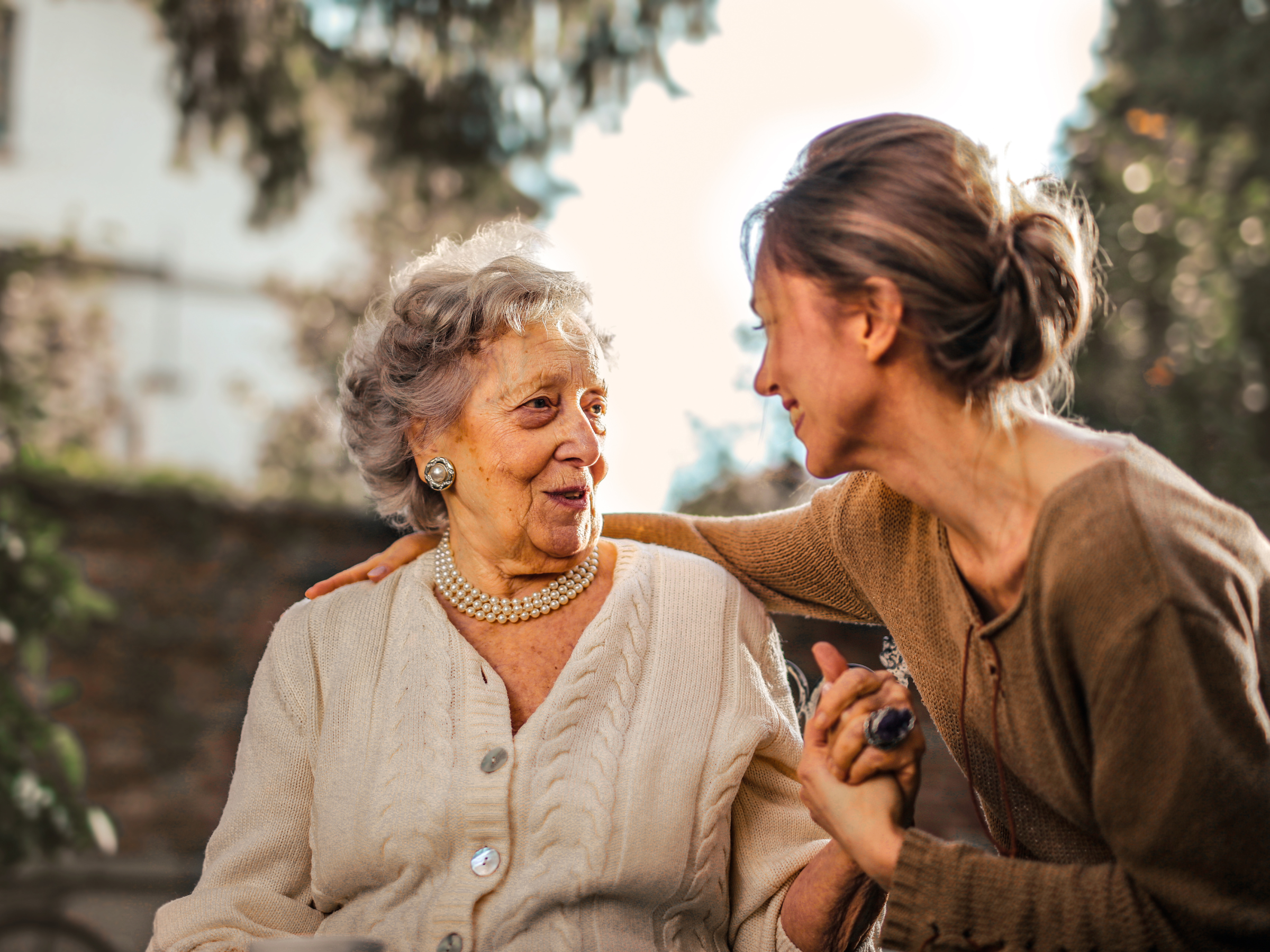 An older woman smiles warmly at her caregiver as they sit together outside, sharing a comforting and supportive moment.