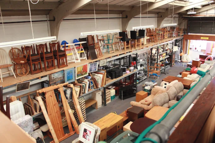 Secondhand furniture store with chairs, tables, artwork, and home decor items on shelves and the floor.