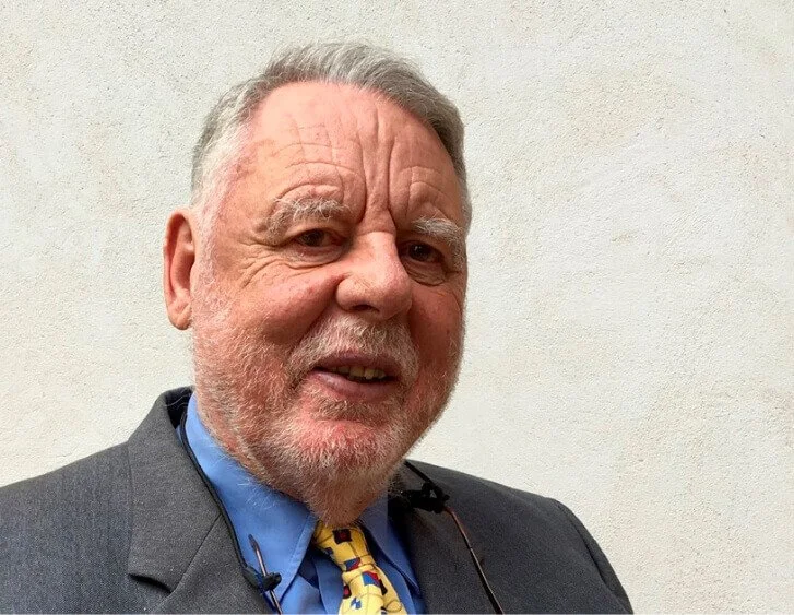 A smiling older man with a beard and mustache, wearing a suit and tie.
