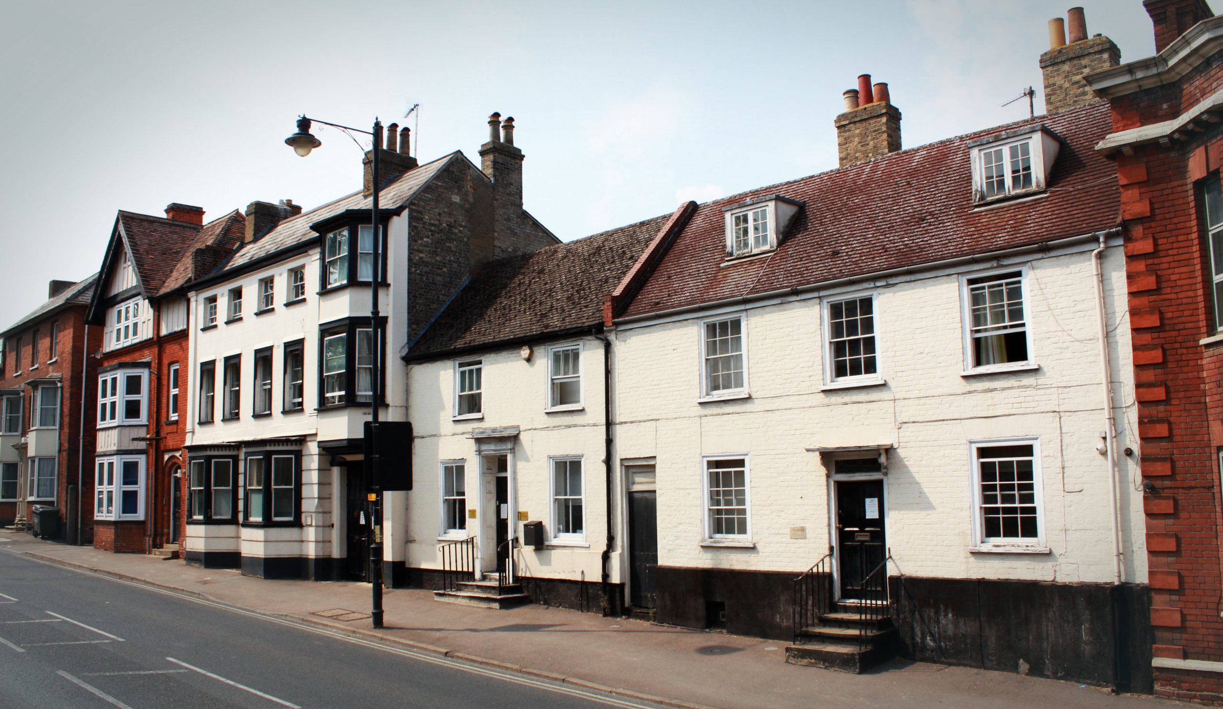 A row of old brick and painted houses on a quiet street with a lamppost in front.