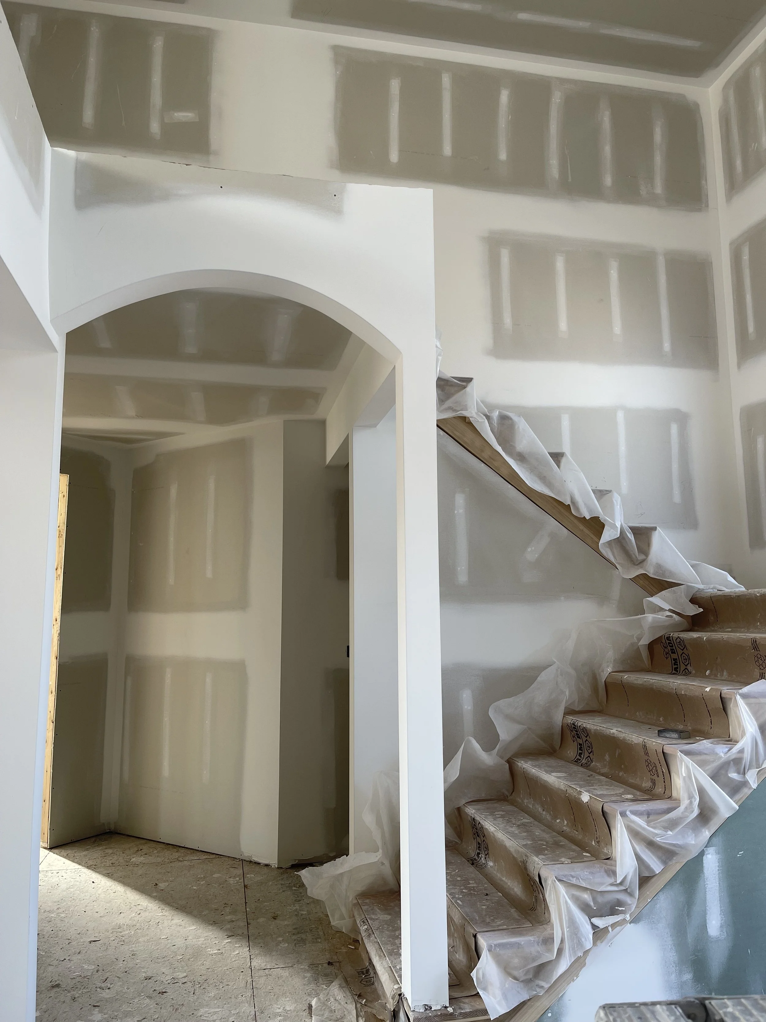 Interior staircase under construction with drywall and protective plastic covering the steps.