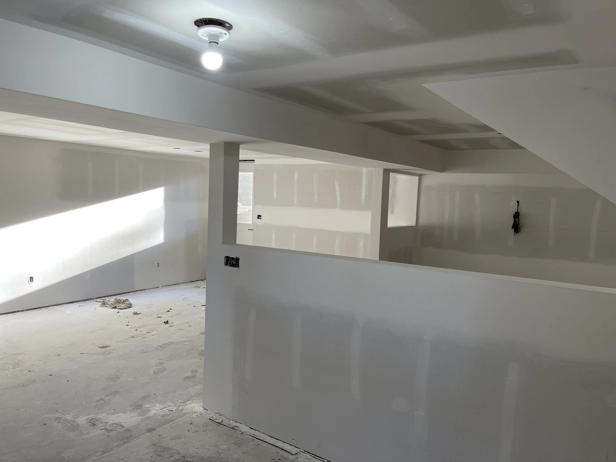 Interior of a building under construction or renovation, with drywall walls and ceiling, exposed electrical outlets, and construction debris on the floor.