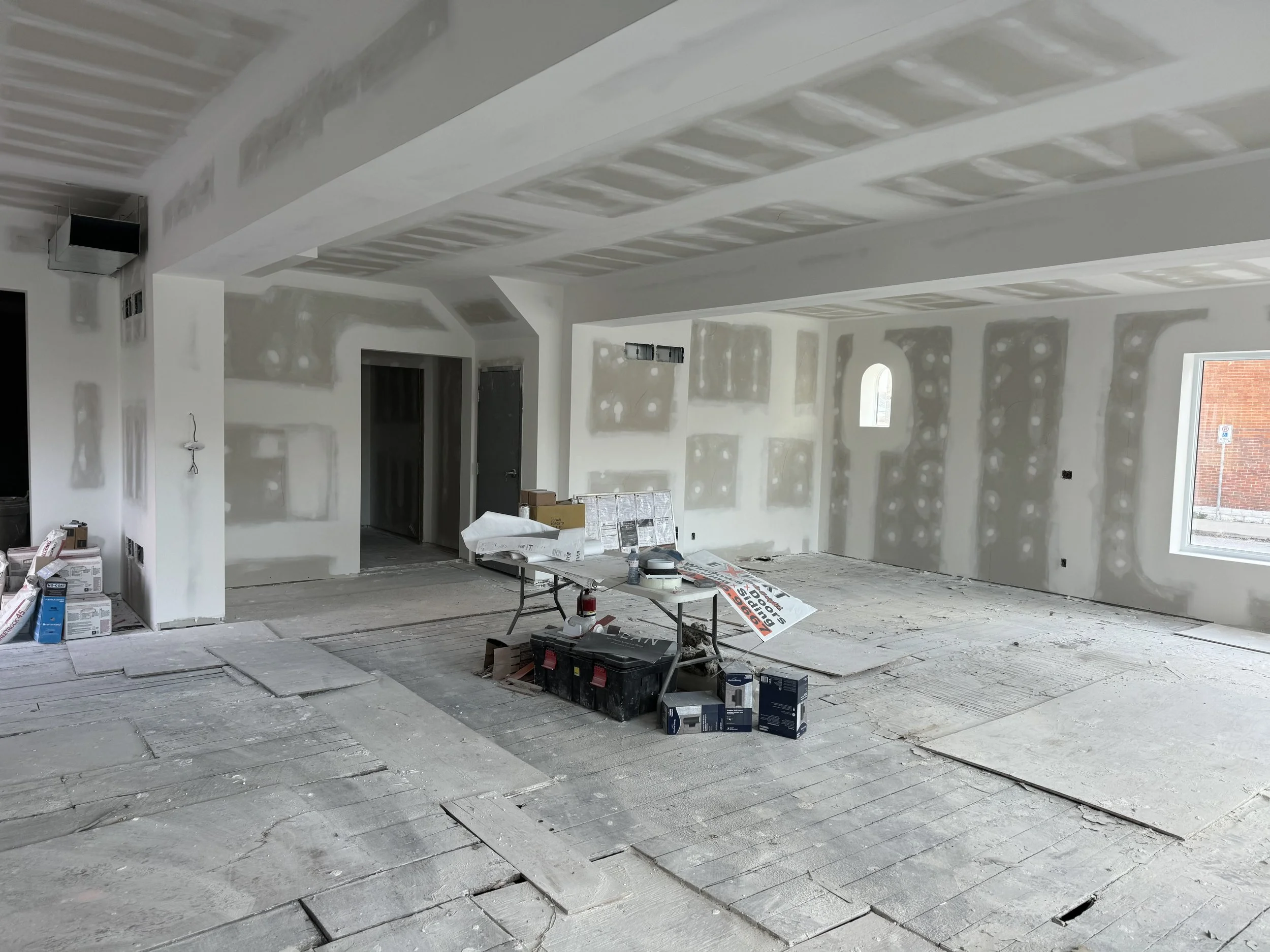 An unfinished room under construction with drywall installed but not yet finished, scattered construction tools and materials, and exposed flooring.