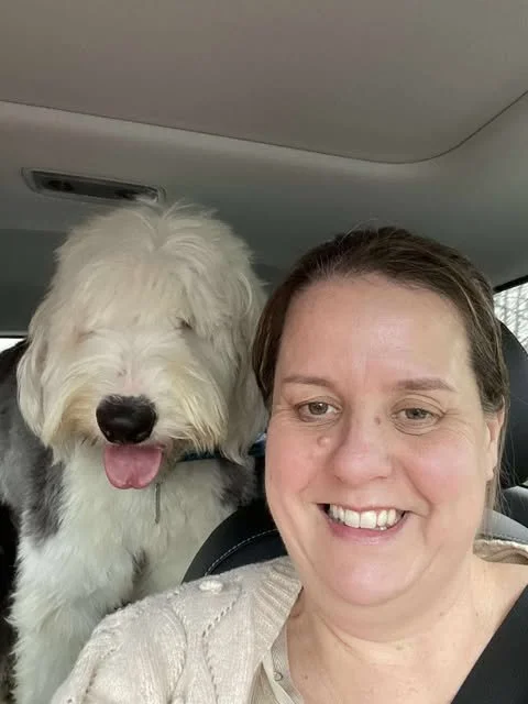 Person smiling in car with large fluffy dog sitting behind her.