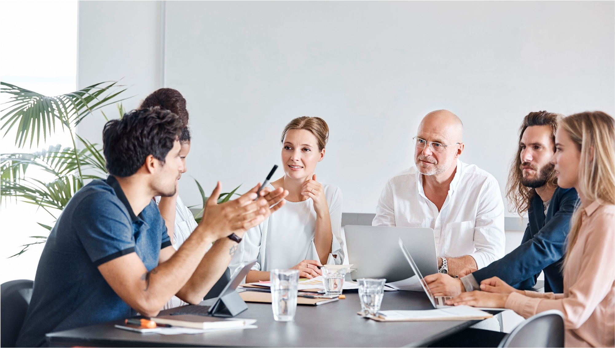 Group of six diverse people having a meeting in a modern conference room with laptops and paperwork on the table.
