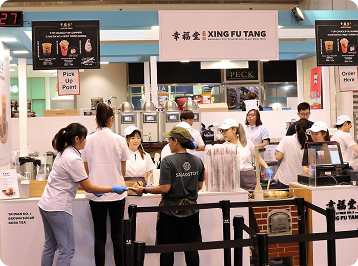 People ordering and serving drinks at a Taiwan bubble tea shop, with signs displaying menu options and pick-up and order points.