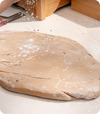 Raw dough sprinkled with flour on a work surface, with a rolling pin in the background.
