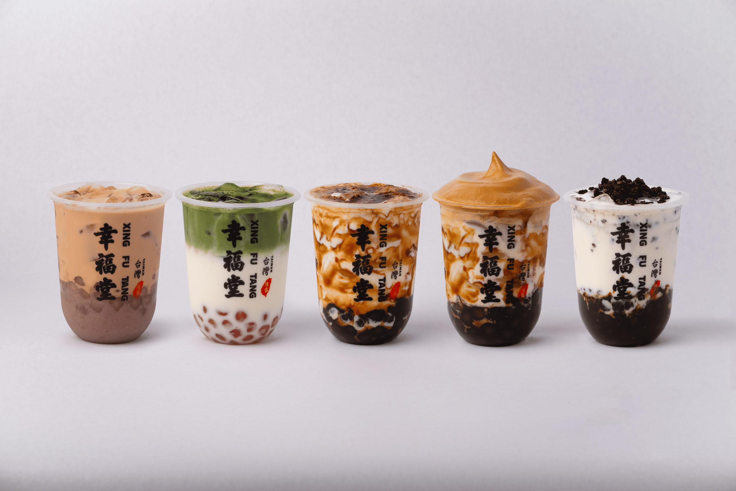 Five cups of bubble tea with various flavors and toppings, lined up on a white surface, against a plain white background.