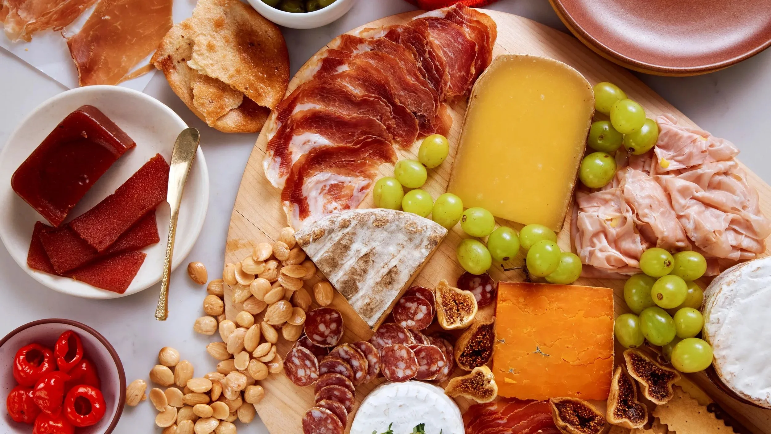 A cheese and charcuterie board with slices of cured meats, various cheeses, grapes, nuts, dried fruits, and crackers.