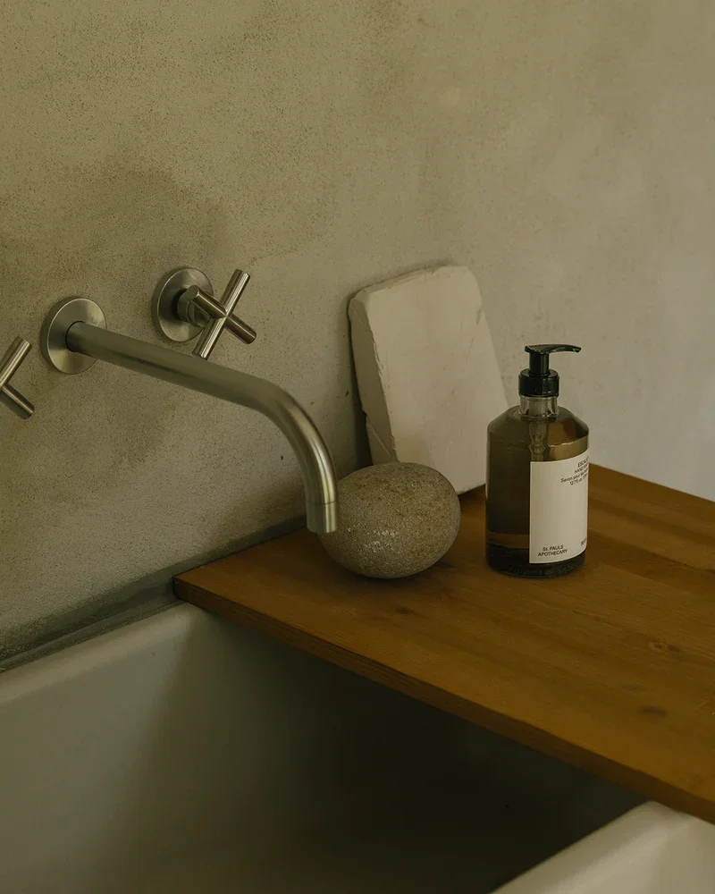 Bathroom sink with a wall-mounted faucet, a soap dispenser, a stone, and a small white tile leaning against the wall.